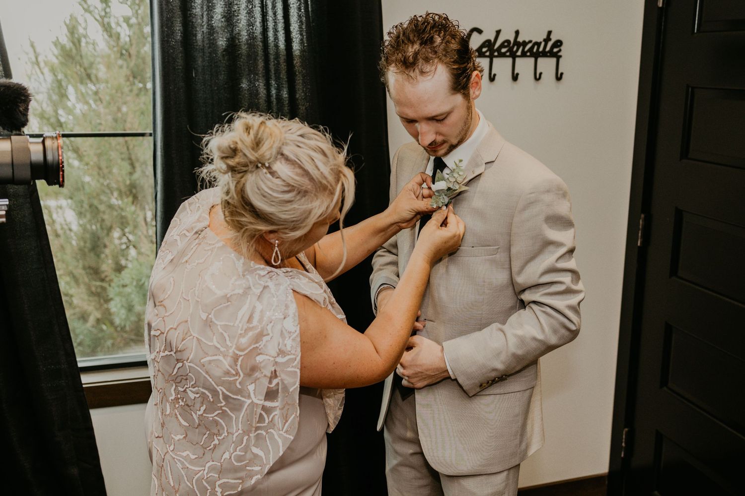 A tender moment as a boutonniere is pinned onto a beige suit during wedding preparations.
