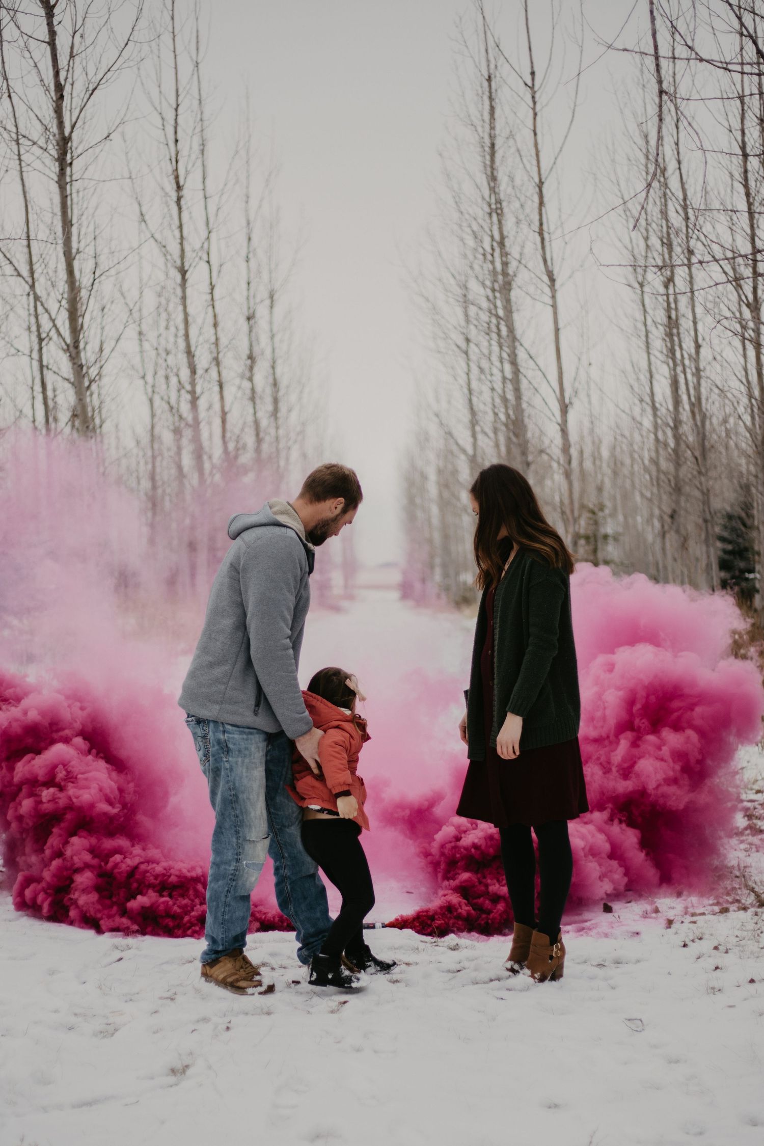 Pink smoke bombs create dramatic effect around a family in winter forest setting.