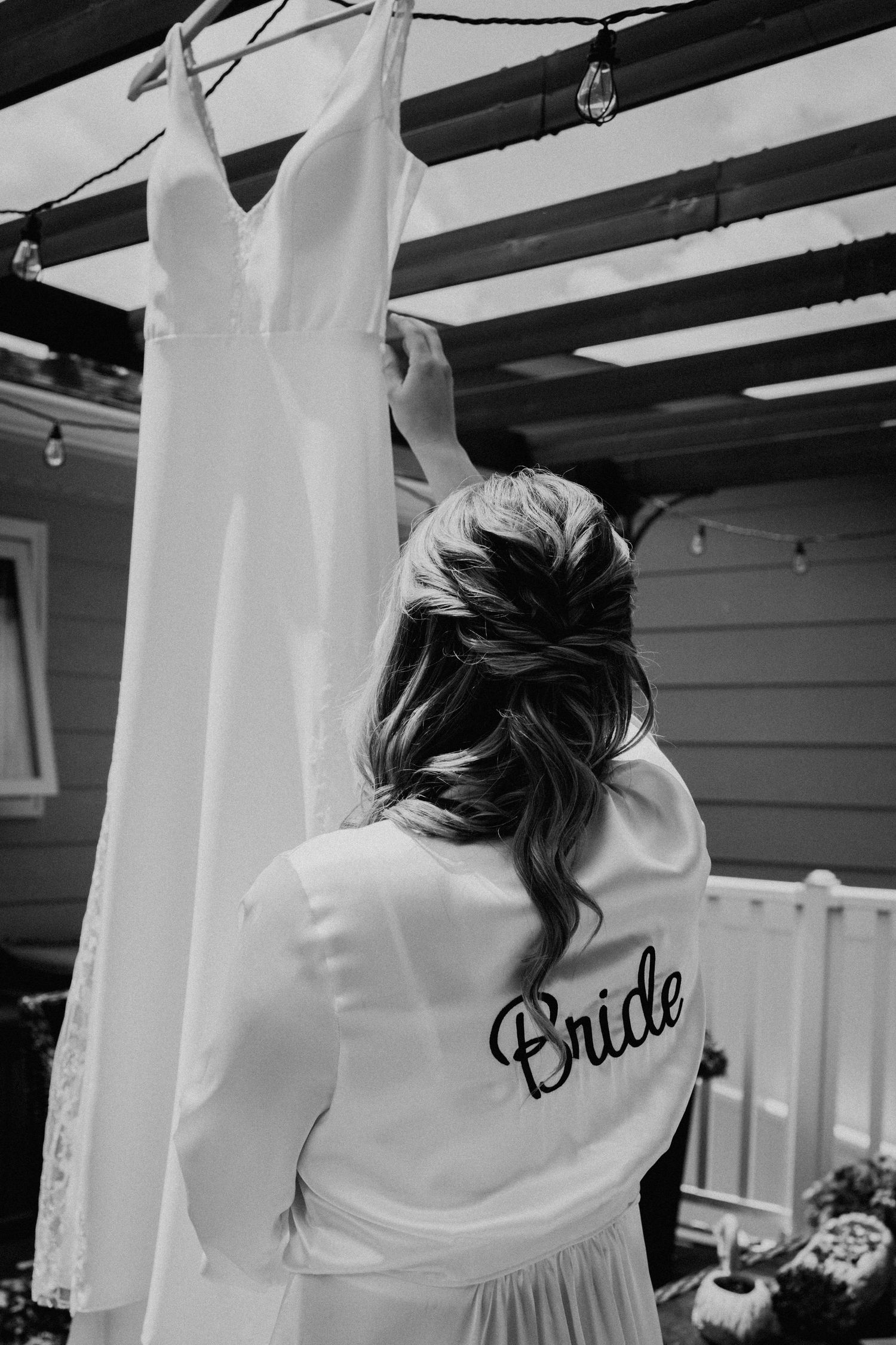 A white wedding gown hanging while someone in a white robe with 'Bride' text adjusts it.