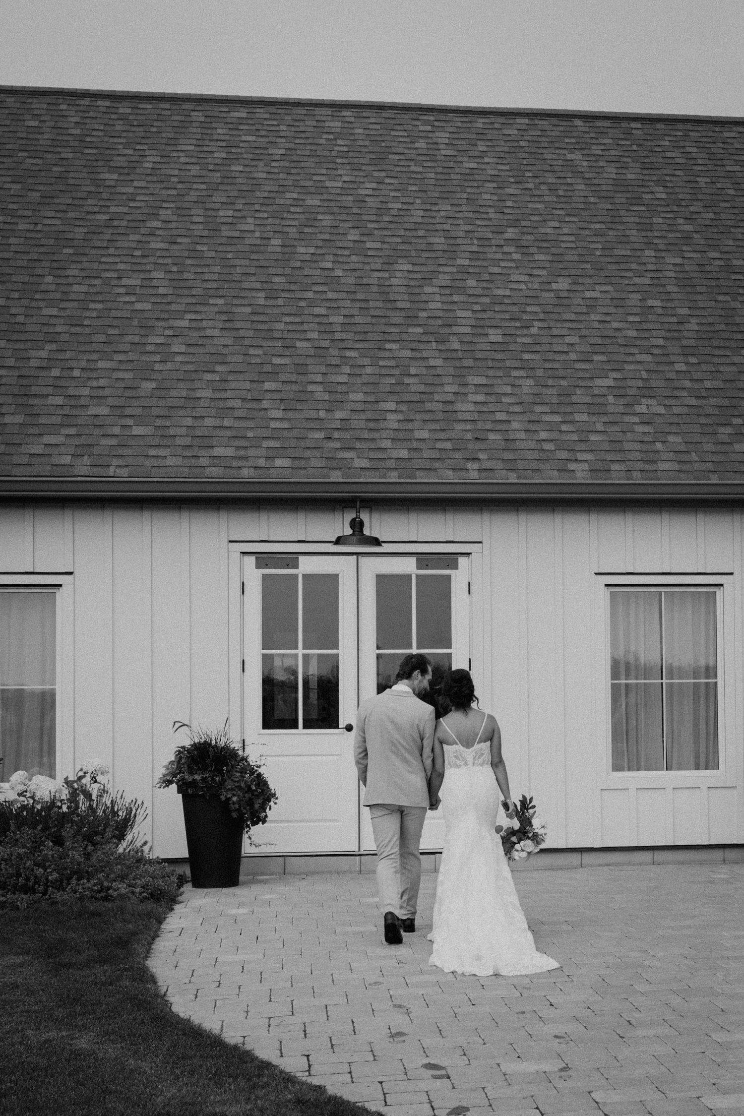 Black and white photo of couple walking towards white farmhouse entrance.
