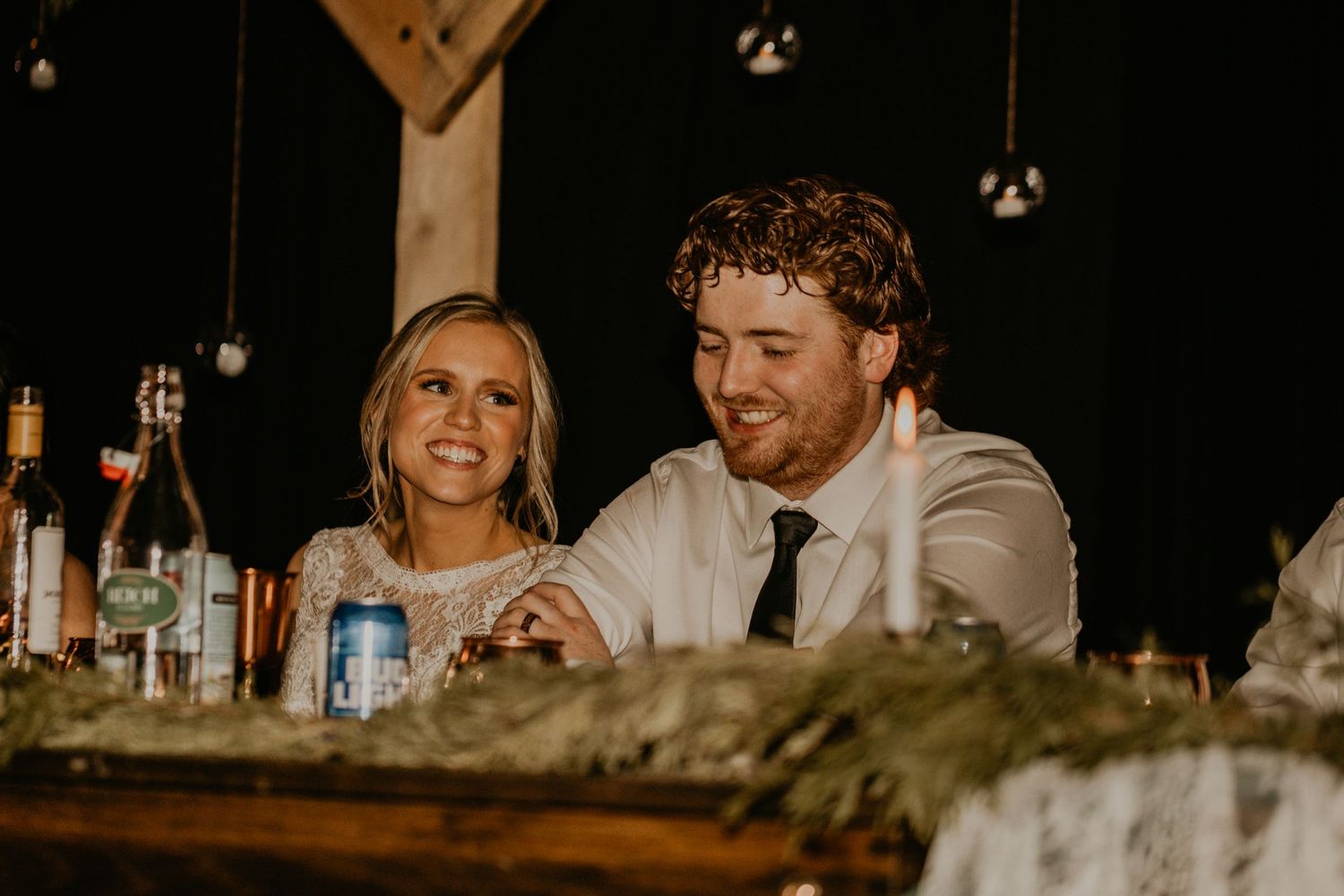 Newlyweds sharing a moment at rustic wooden reception table.