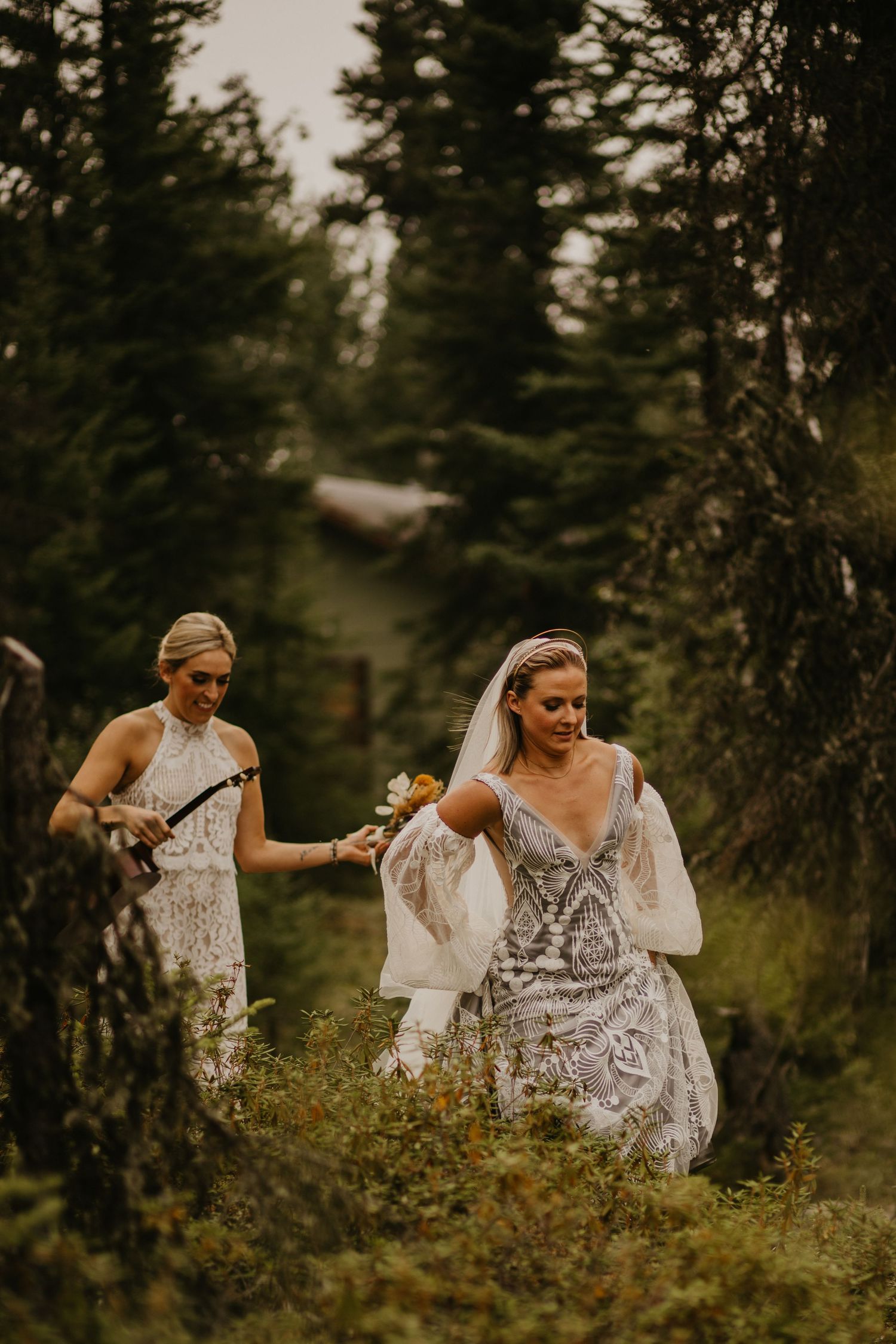 A bride in lace dress walks through a forest path with her wedding party.