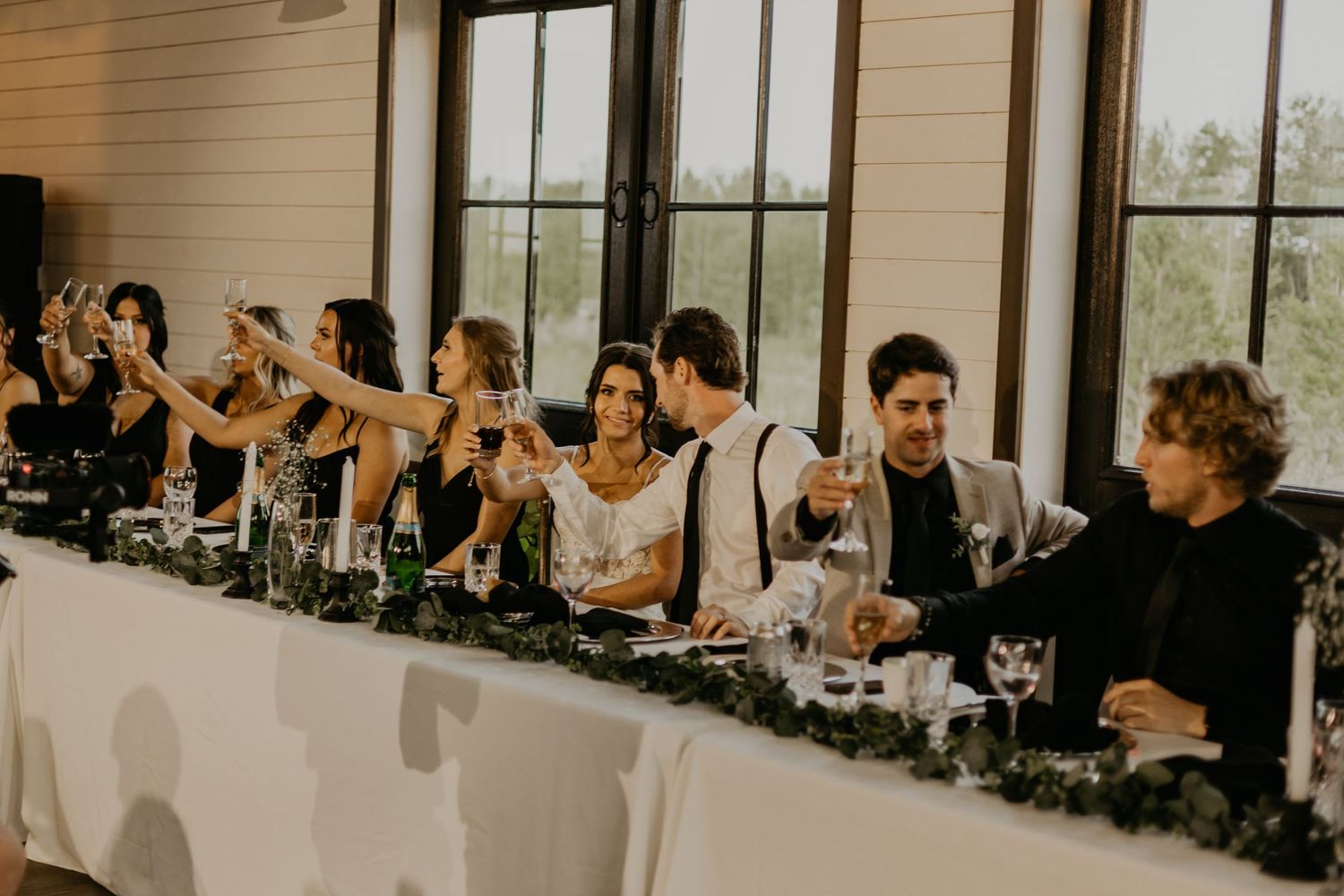 Wedding party raises glasses in celebration toast at decorated reception table.