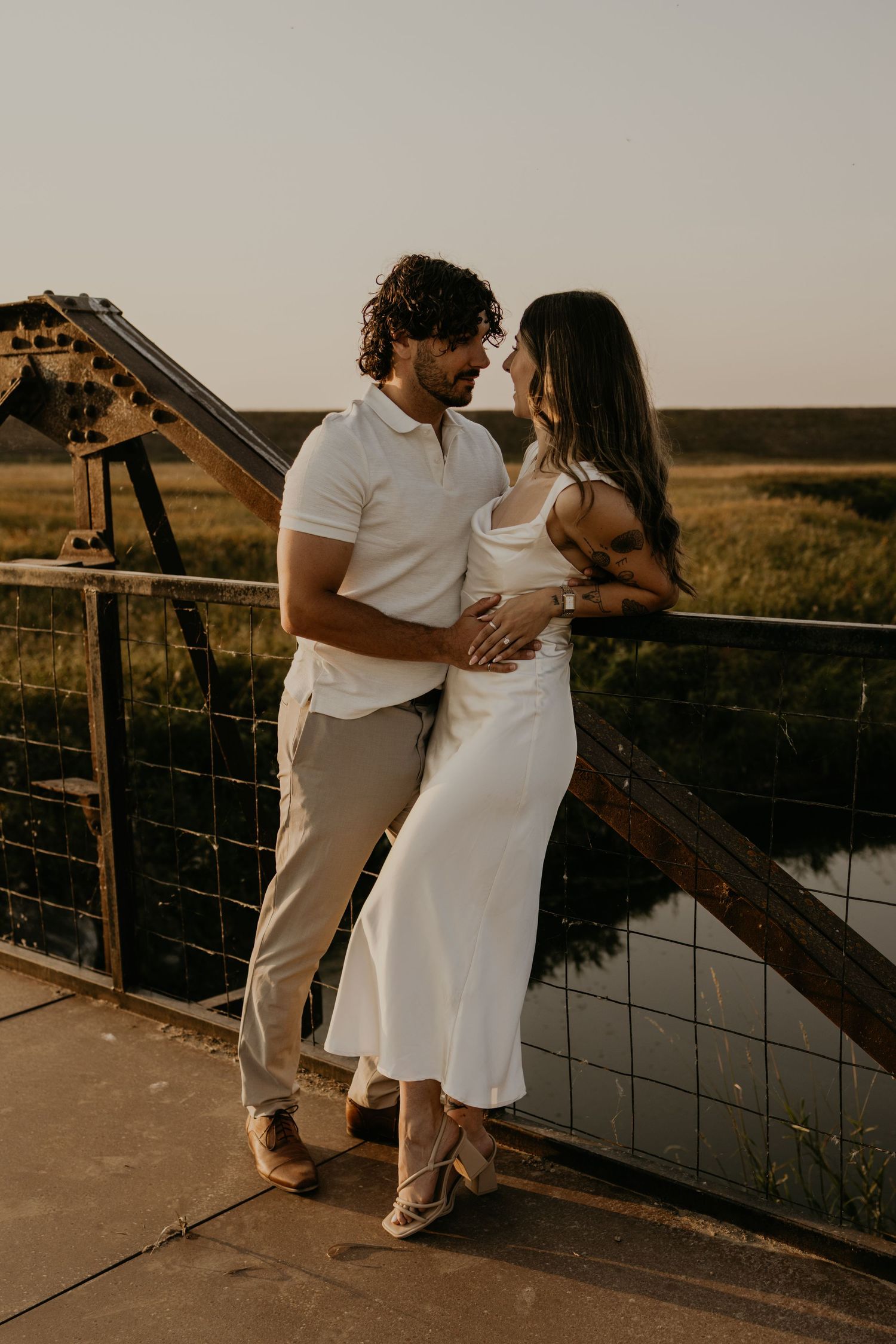 Romantic couple embraces at sunset on wooden deck overlooking scenic landscape.