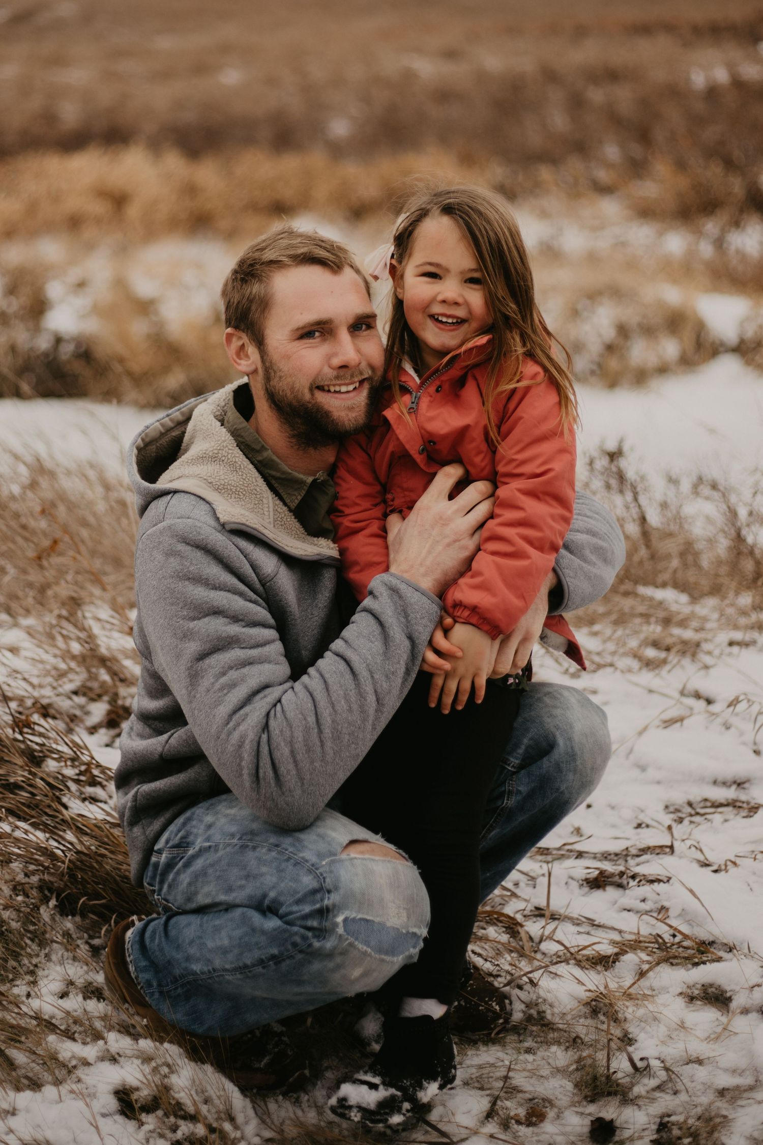 A joyful portrait against a winter landscape with snow patches and brown grass.