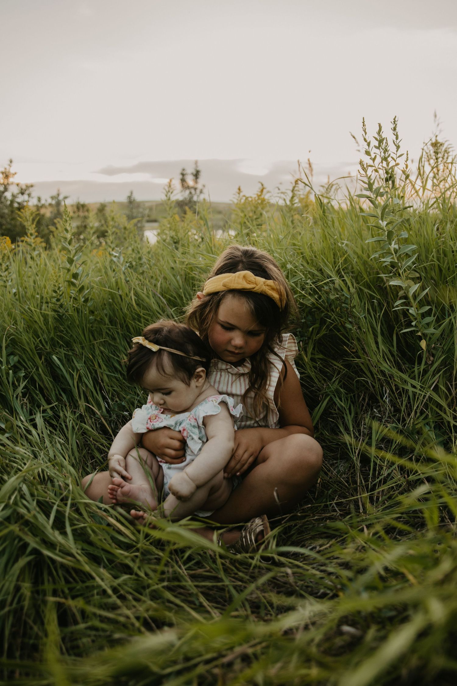 Intimate family moment captured in tall grass during sunset.