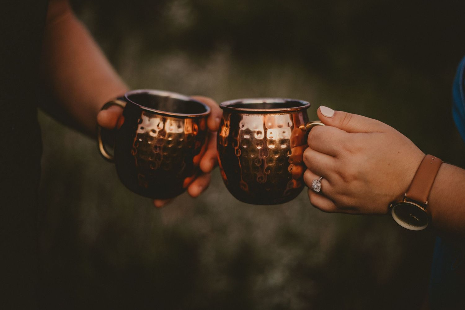Two copper mugs clinking together in a toast at dusk with candlelight glowing inside.