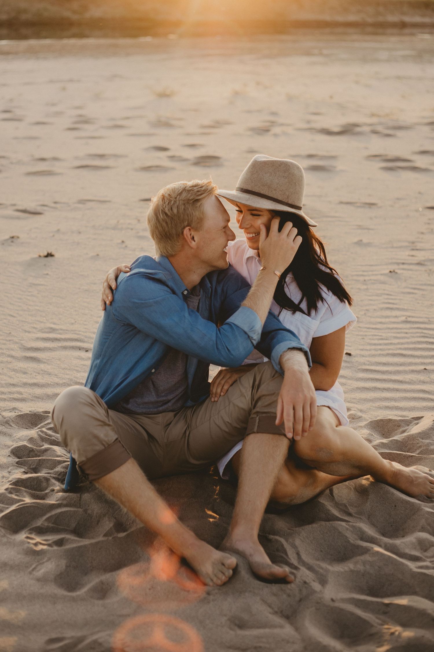 A sweet moment between a couple sitting on sandy beach during golden hour.