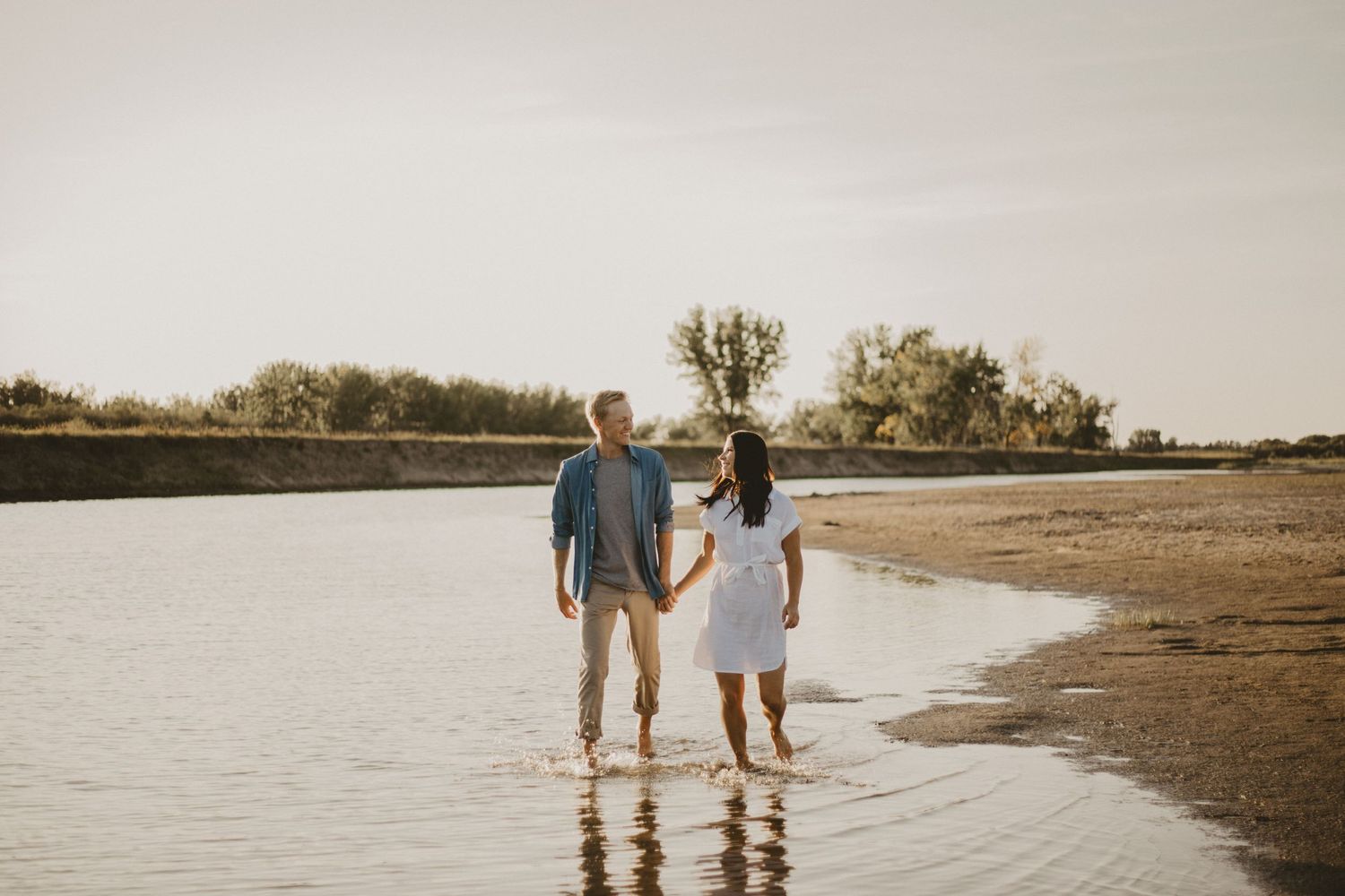Couple stands together at water's edge during sunset photo session.