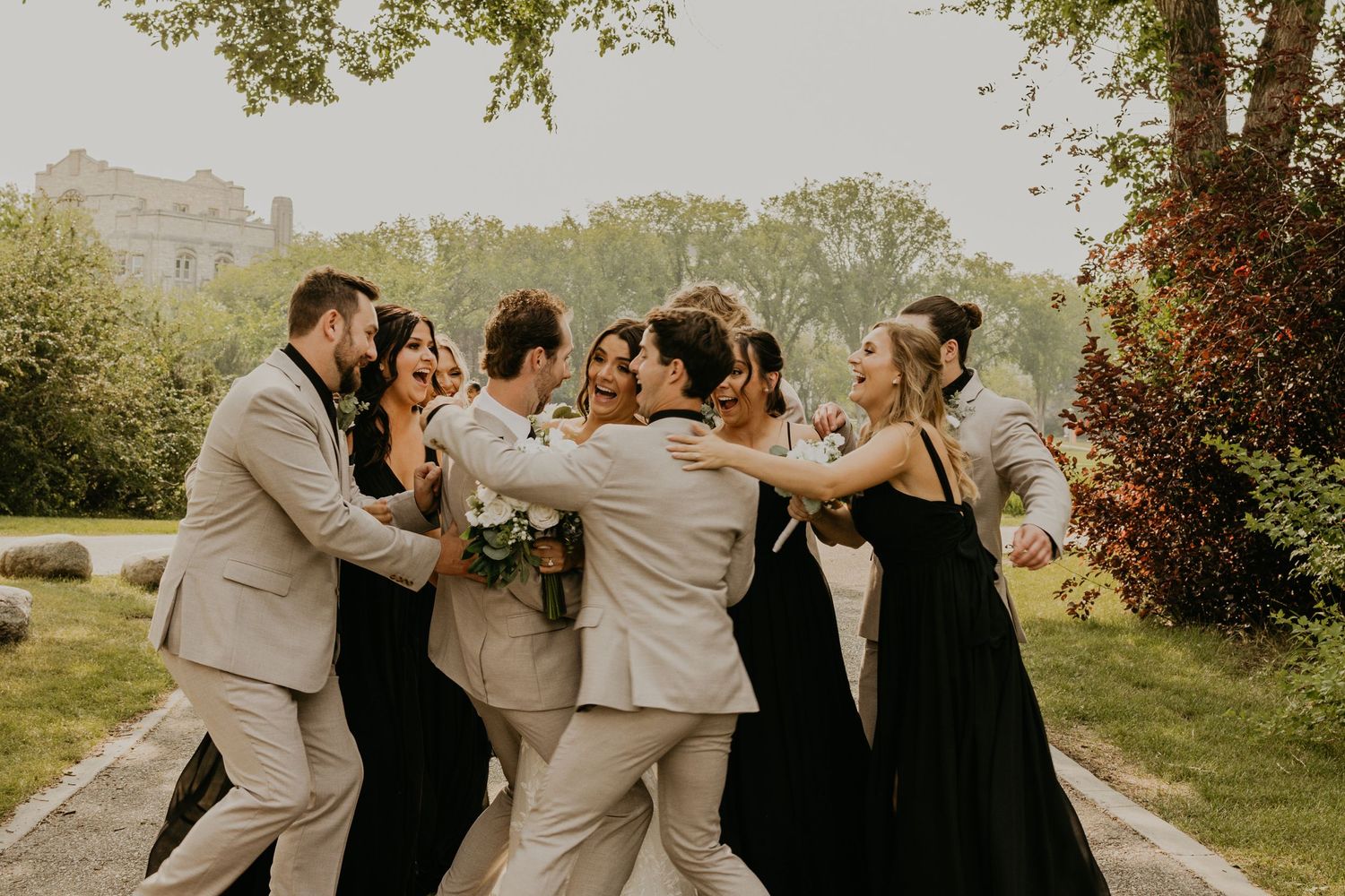 Wedding party laughing and dancing together outdoors in formal attire.
