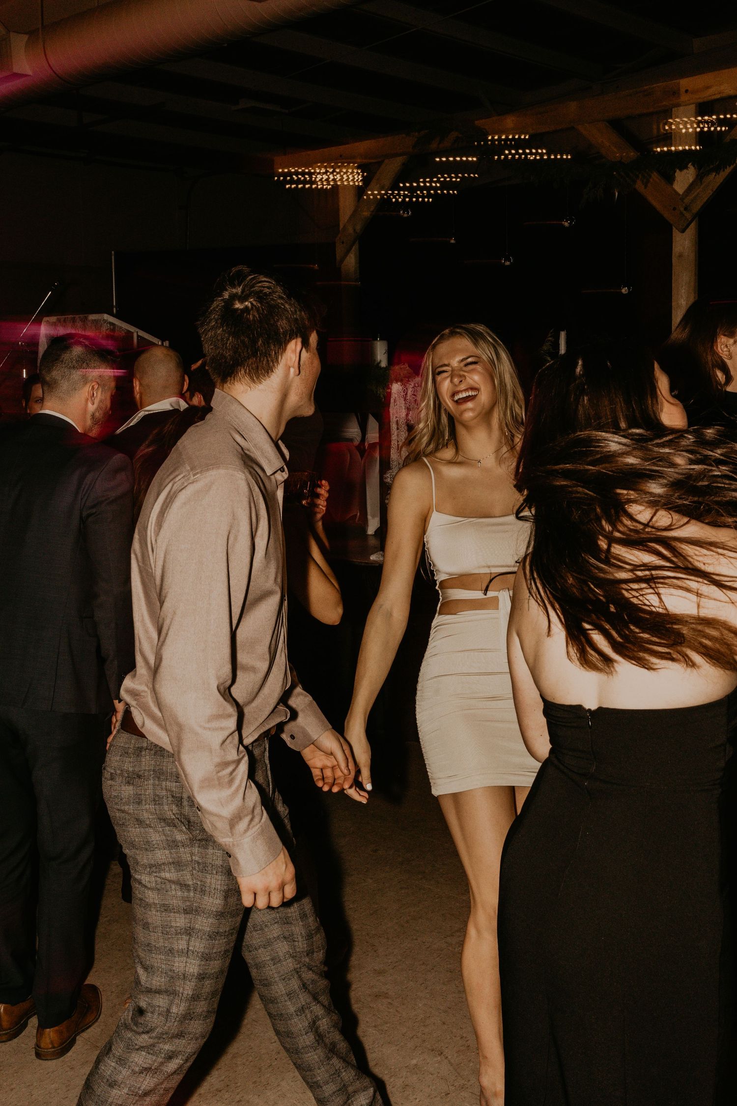 Guests dancing energetically at a nighttime party venue with string lights overhead.