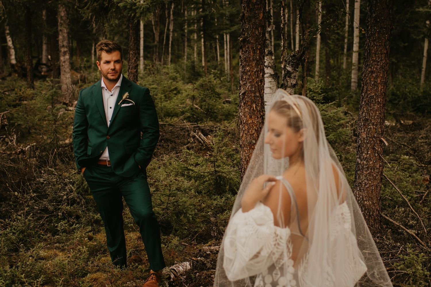 Wedding couple in emerald suit and lace dress pose separately in forest landscape.
