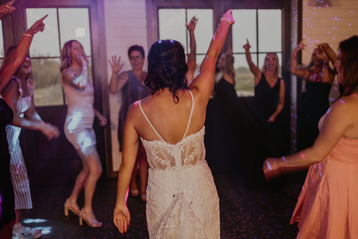Wedding party dancing with arms raised on a lively dance floor.