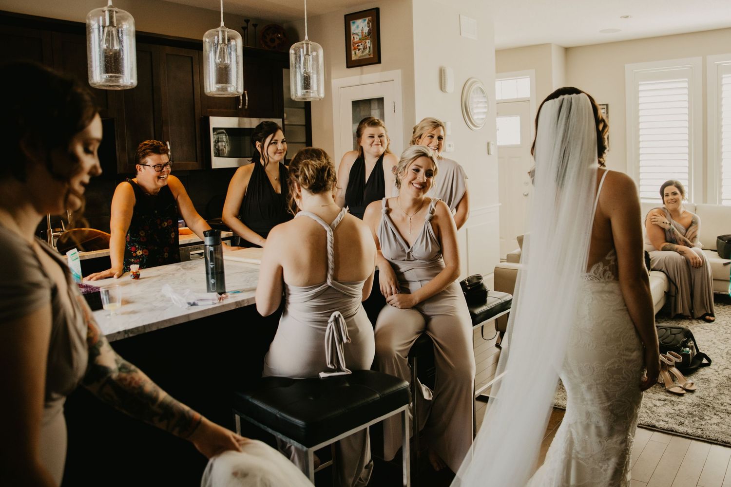 Getting ready scene with wedding party gathered around vanity mirror in preparation room.