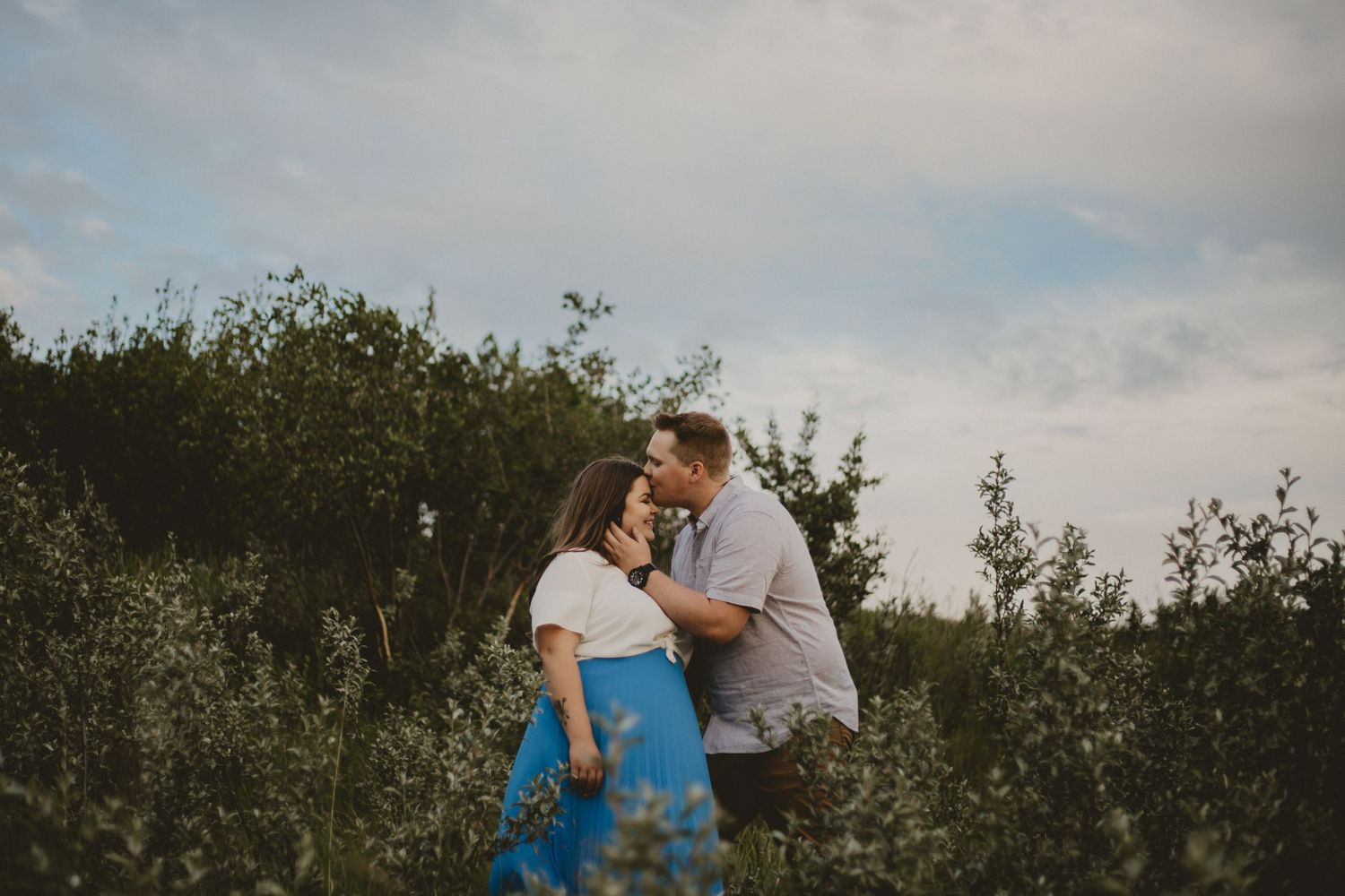 A romantic couple shares an intimate moment among wildflowers and greenery at dusk.