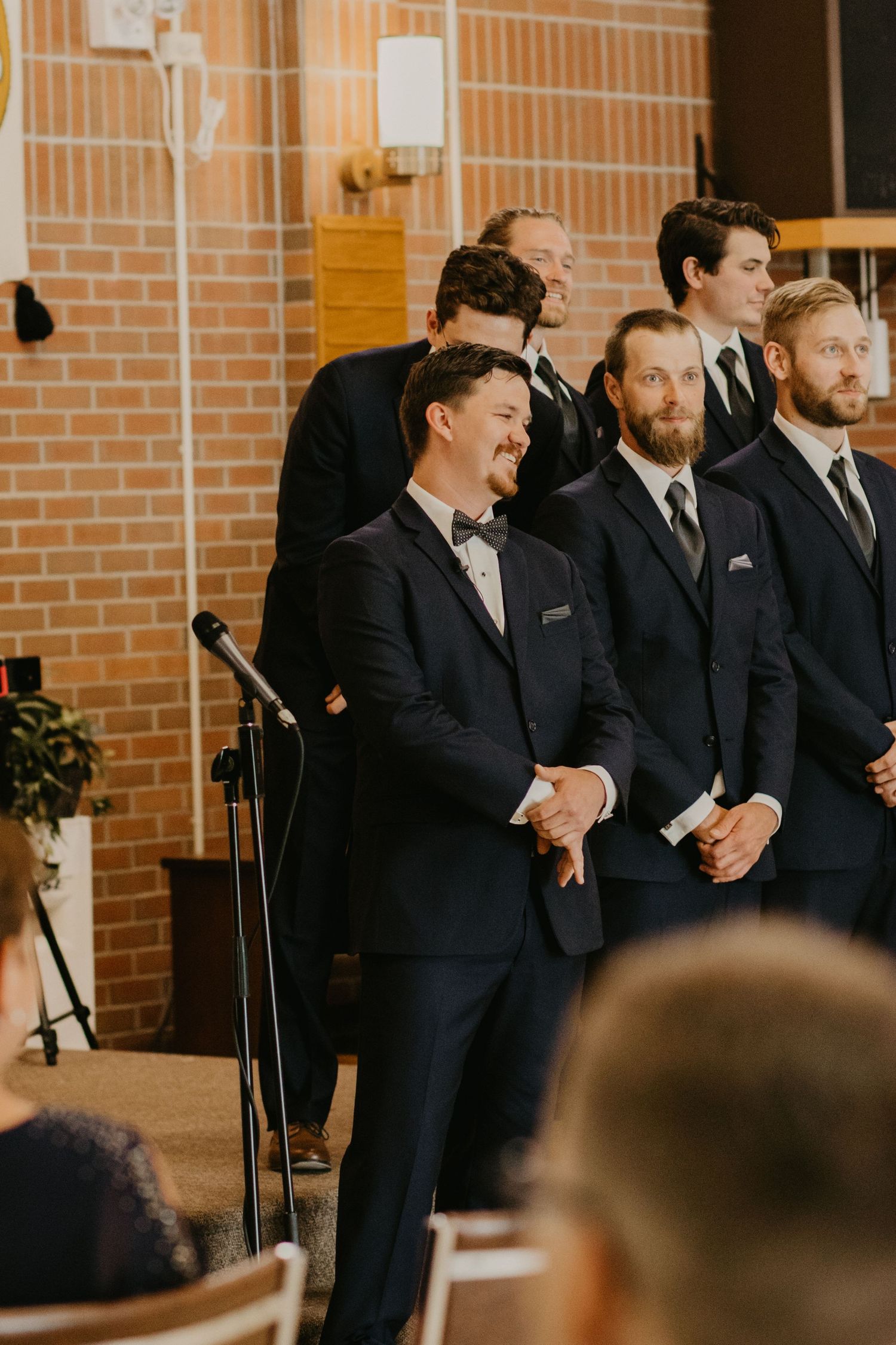 Groomsmen in dark suits stand in a line at a wedding ceremony.