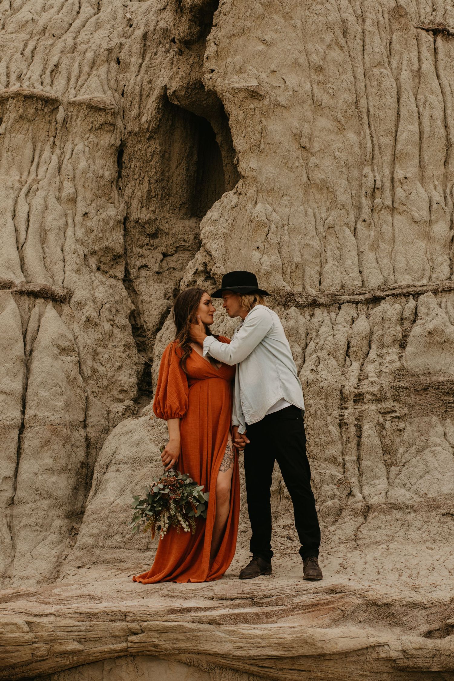 A romantic couple poses against dramatic limestone cliffs wearing formal attire.