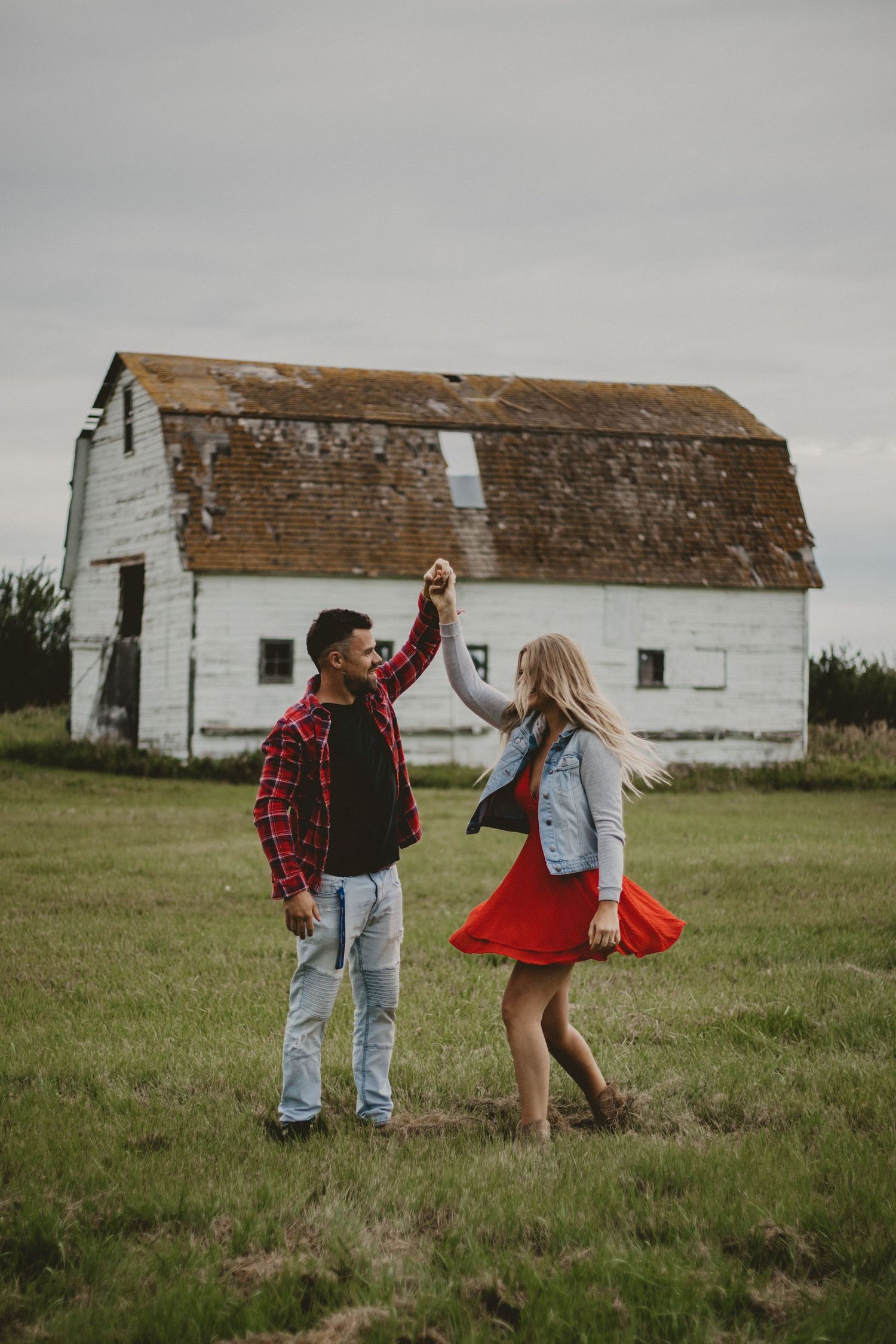 A couple dancing and twirling in front of a weathered white barn.
