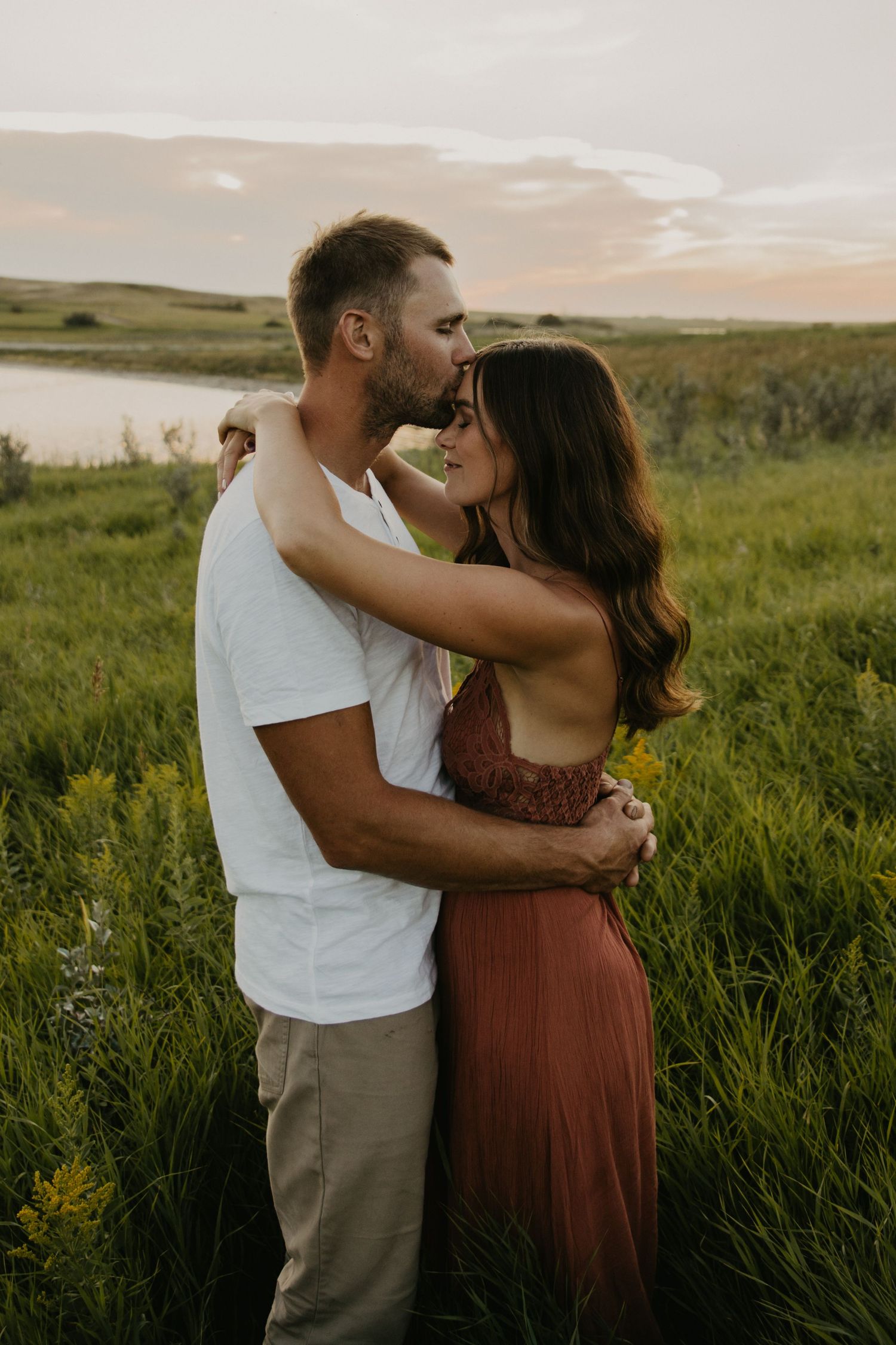 An intimate moment between a couple standing in tall grass during golden hour.