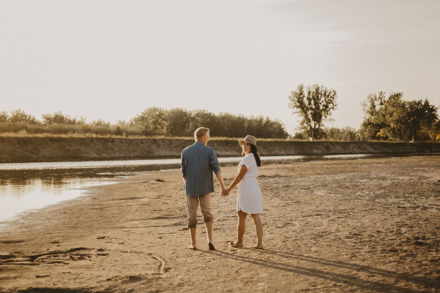 Couple strolls along sandy beach during golden hour photoshoot.