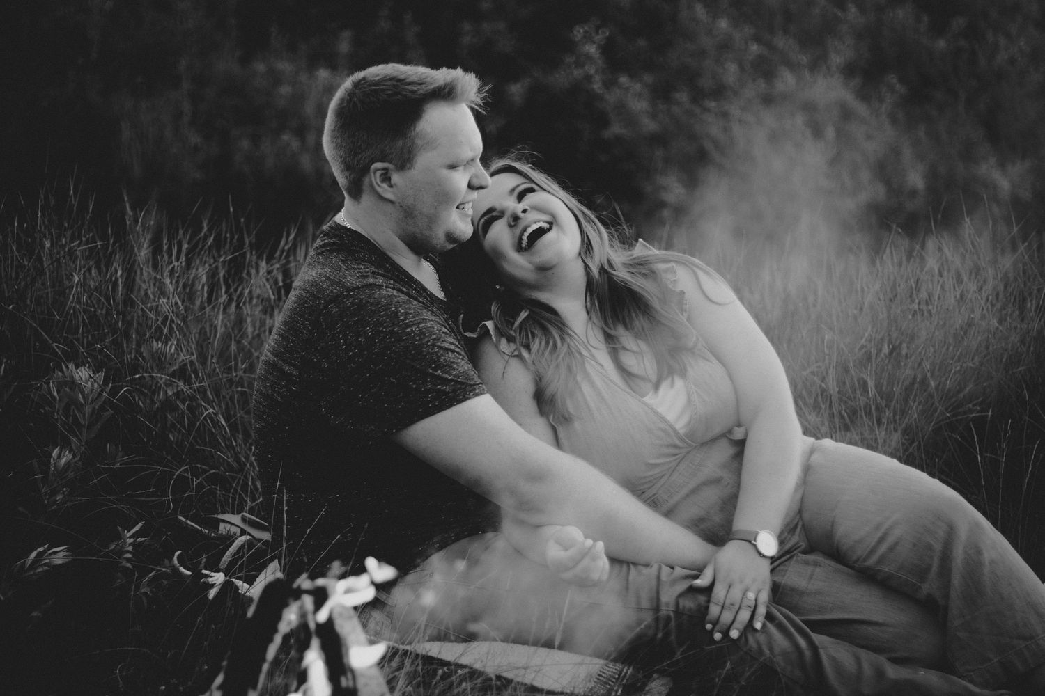 A candid black and white photo of a couple laughing together in a grassy field.