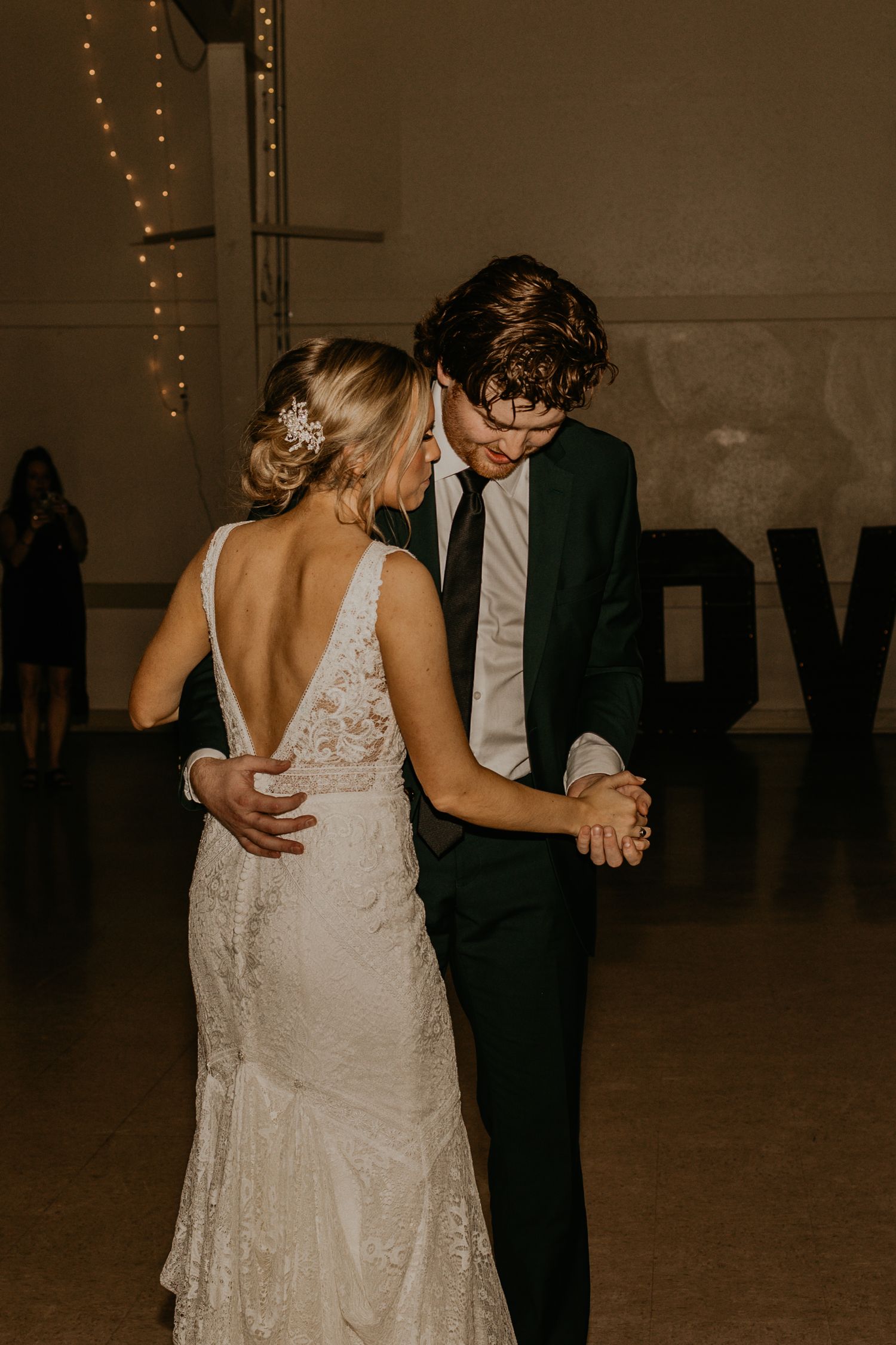 A romantic first dance between newlyweds in a dimly lit reception hall with string lights and LOVE signage.