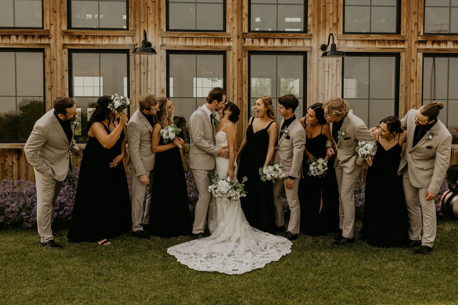 Wedding party shares a joyful candid moment together outside a rustic venue.