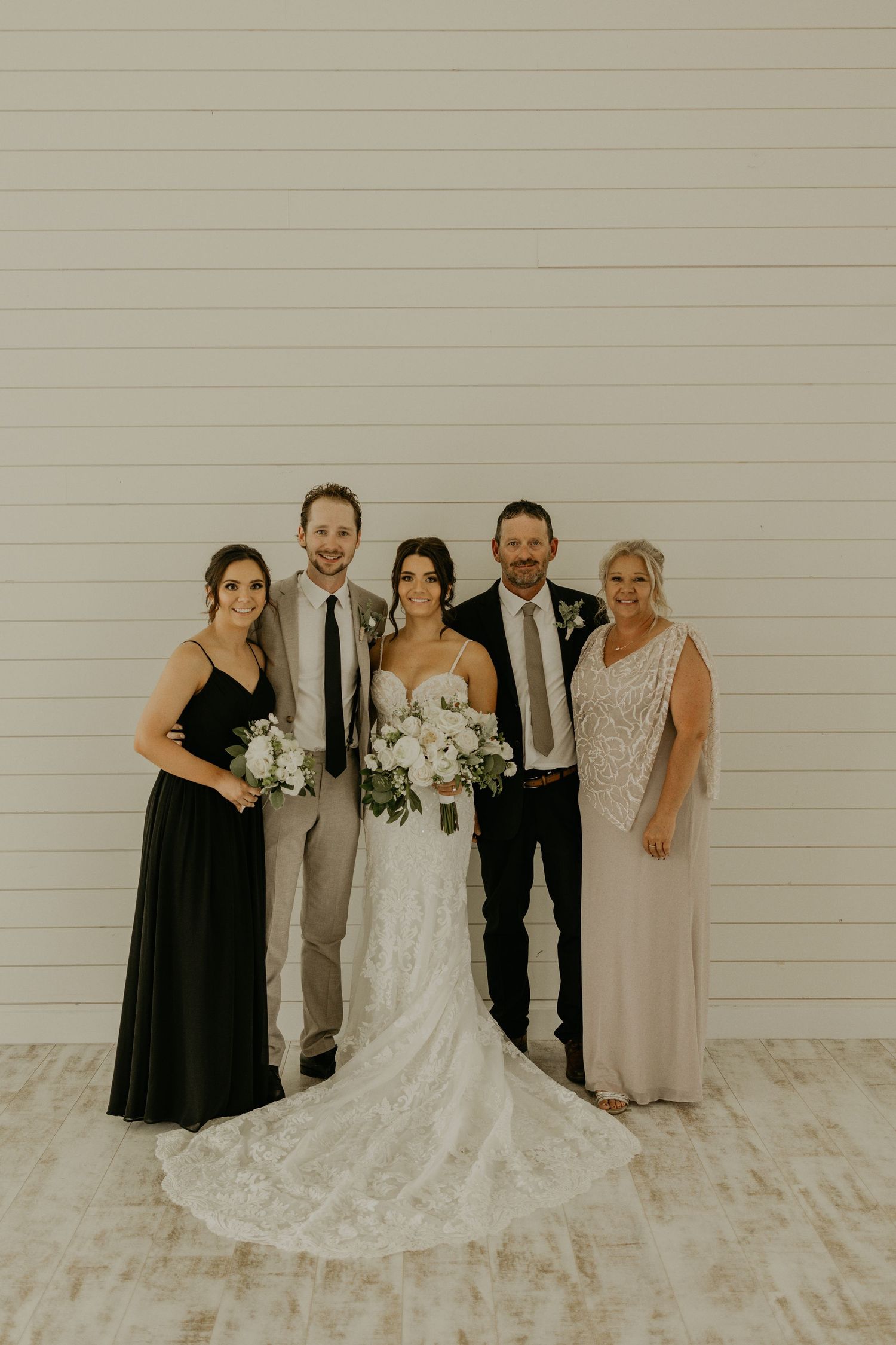 Small wedding group poses formally against white wall in mix of evening wear and formal attire.