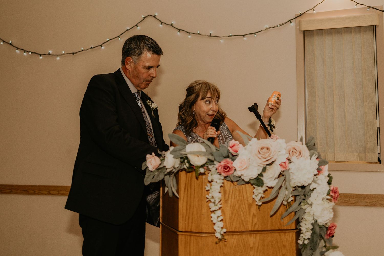 Wedding speeches being delivered at a wooden podium adorned with white floral arrangements.