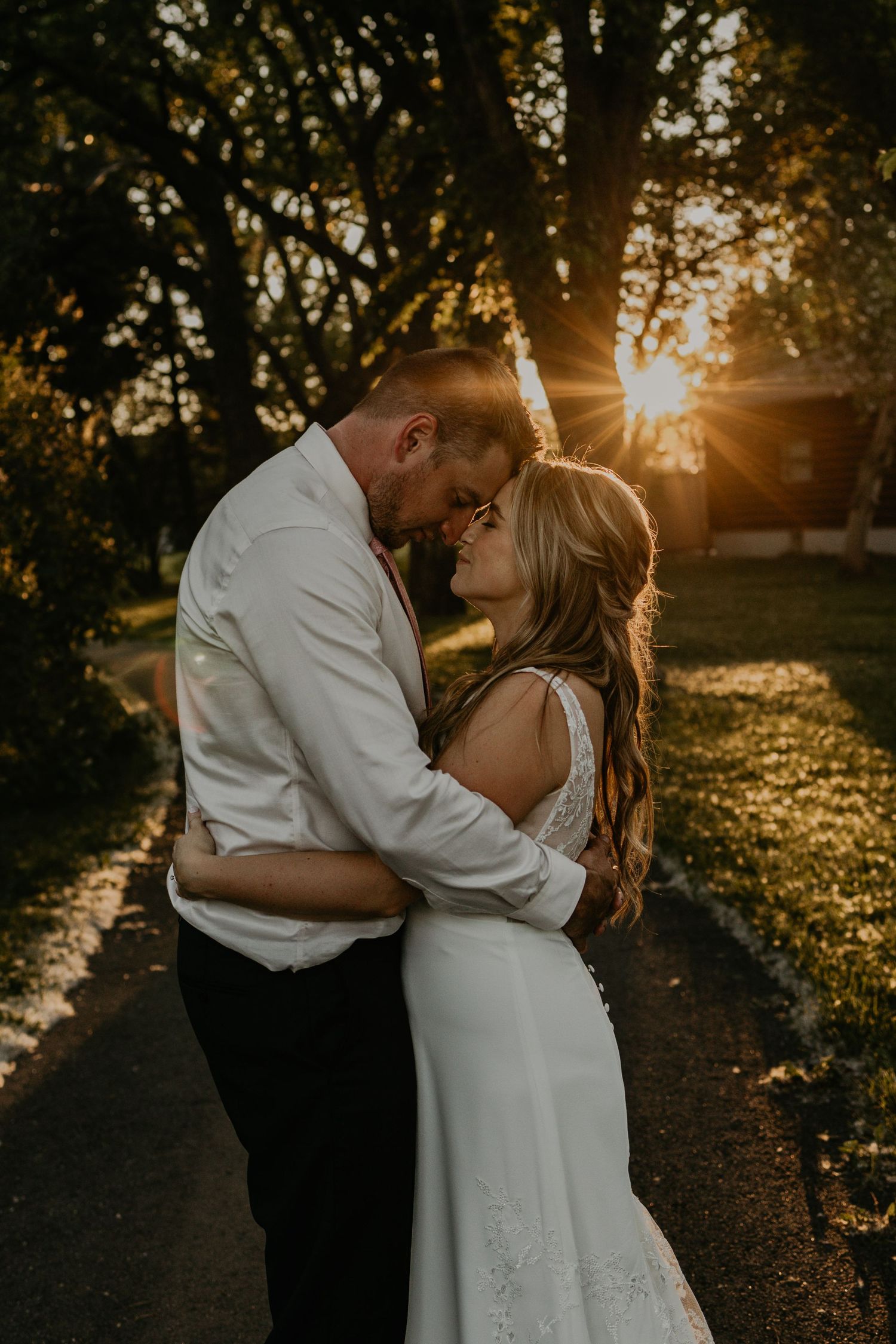 A romantic sunset embrace on a tree-lined path during a wedding photoshoot.