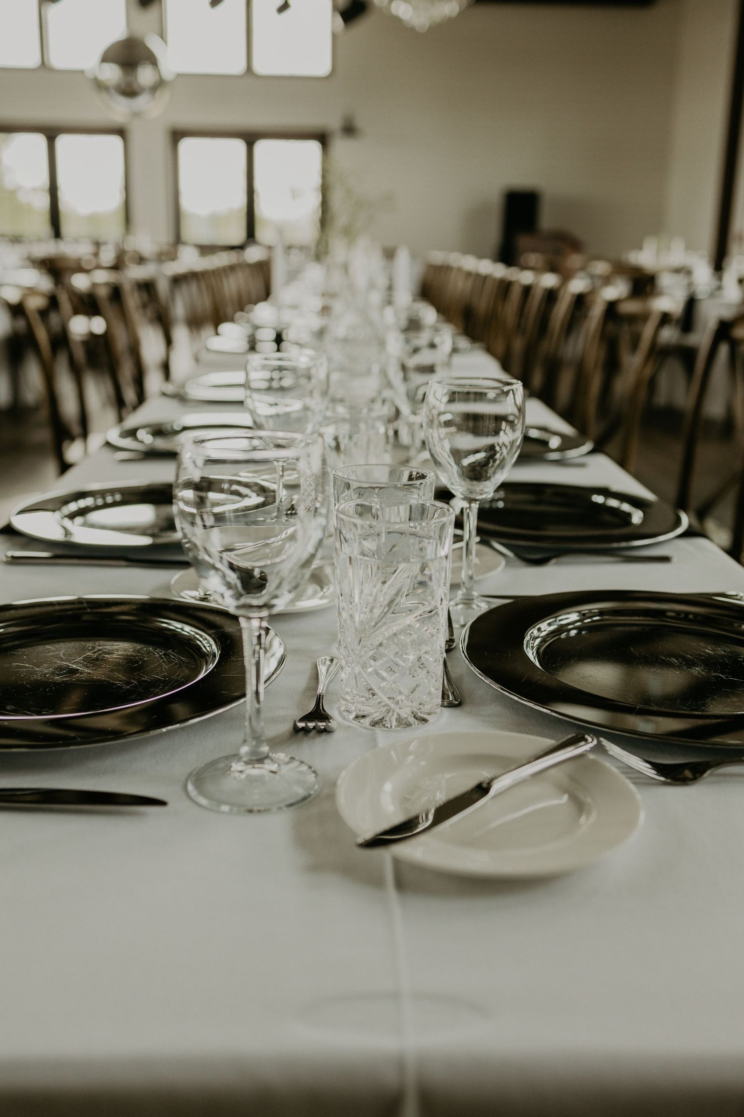 Close-up of formal place settings with wine glasses and black plates on a white tablecloth.