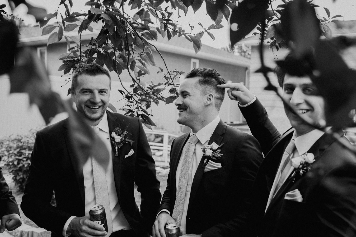 Black and white candid shot of groomsmen laughing together outdoors.
