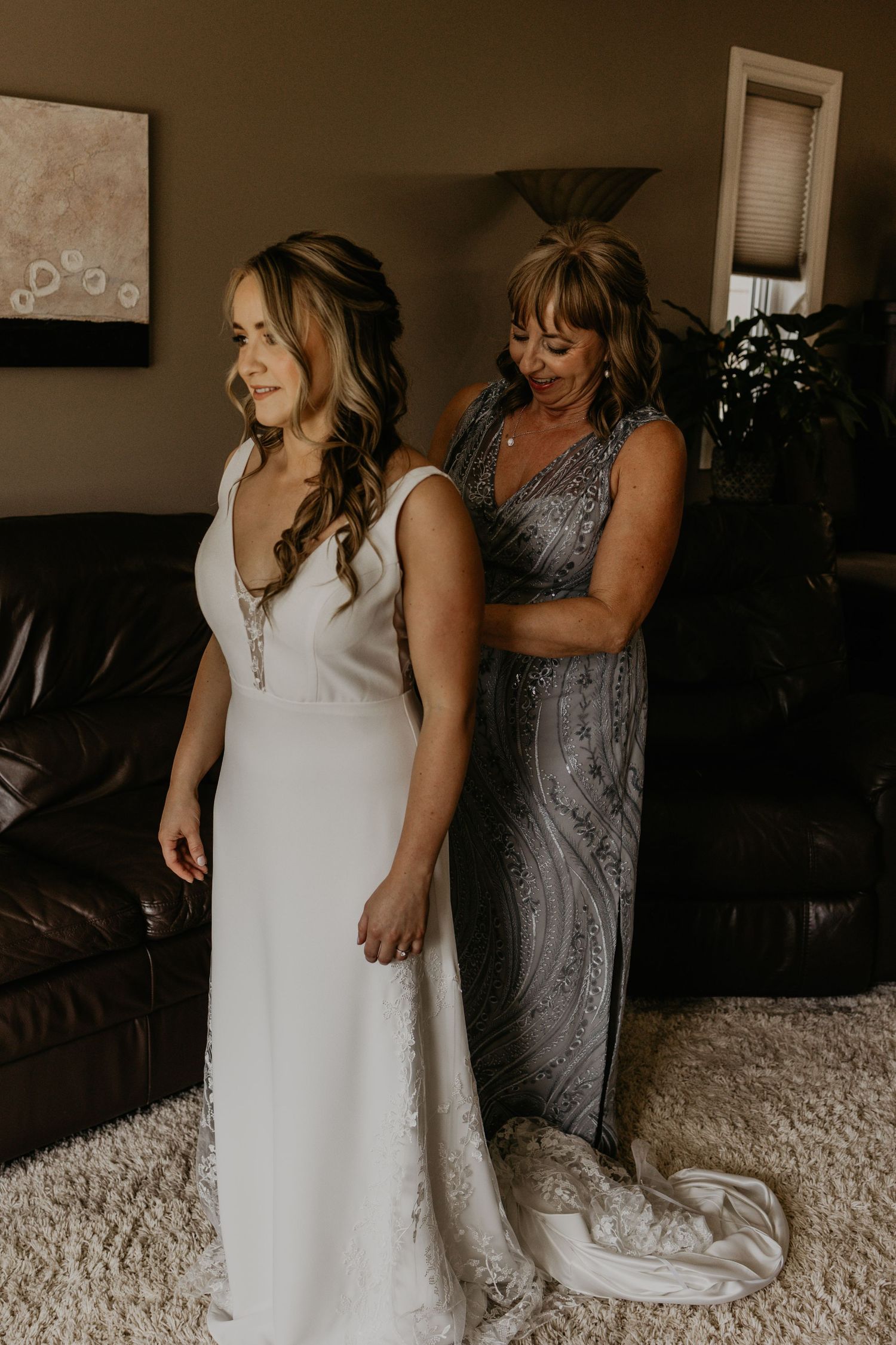 A bridal gown being adjusted in a dimly lit room with leather furniture.