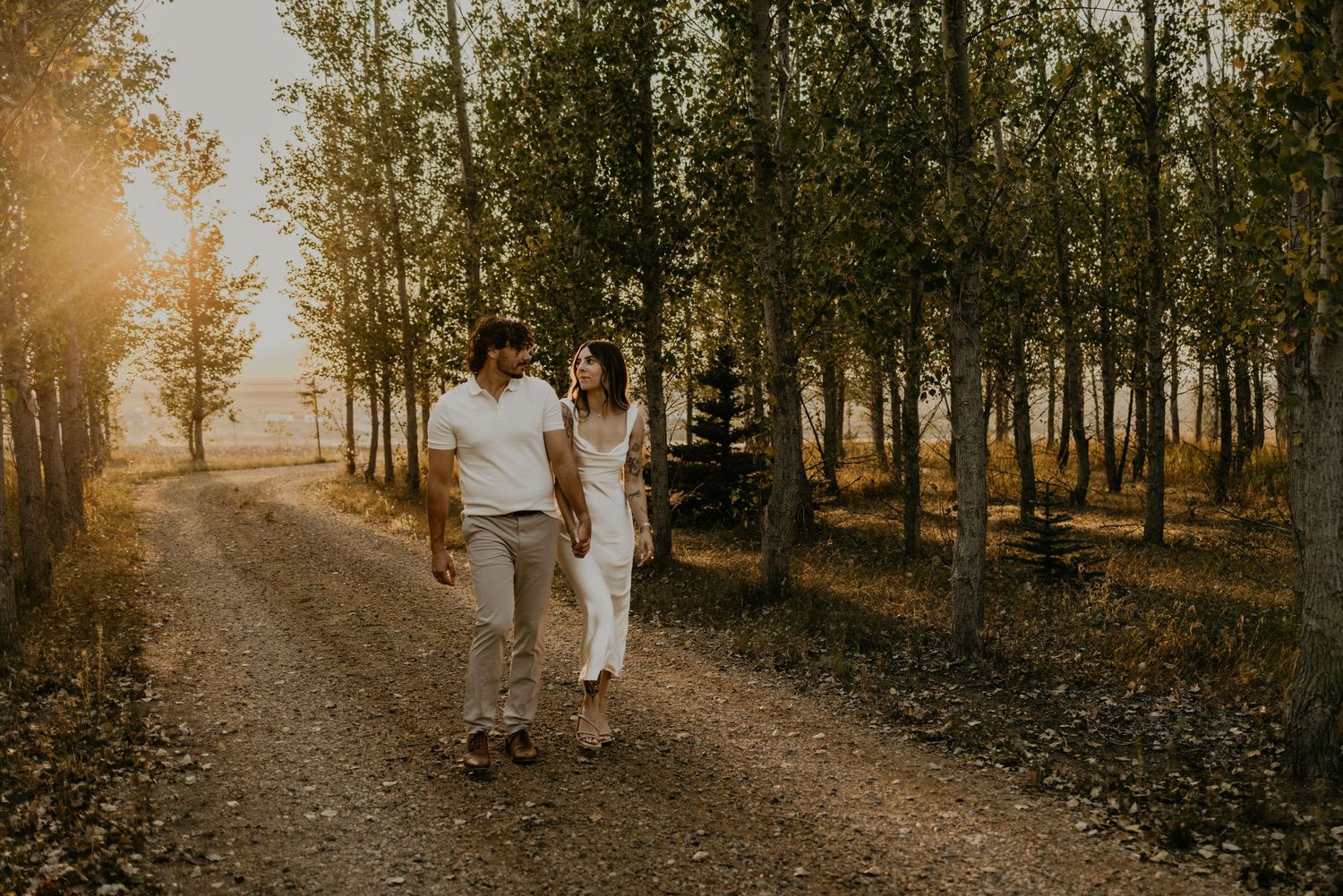 People walking through tree-lined path with golden sunset light filtering through autumn leaves.
