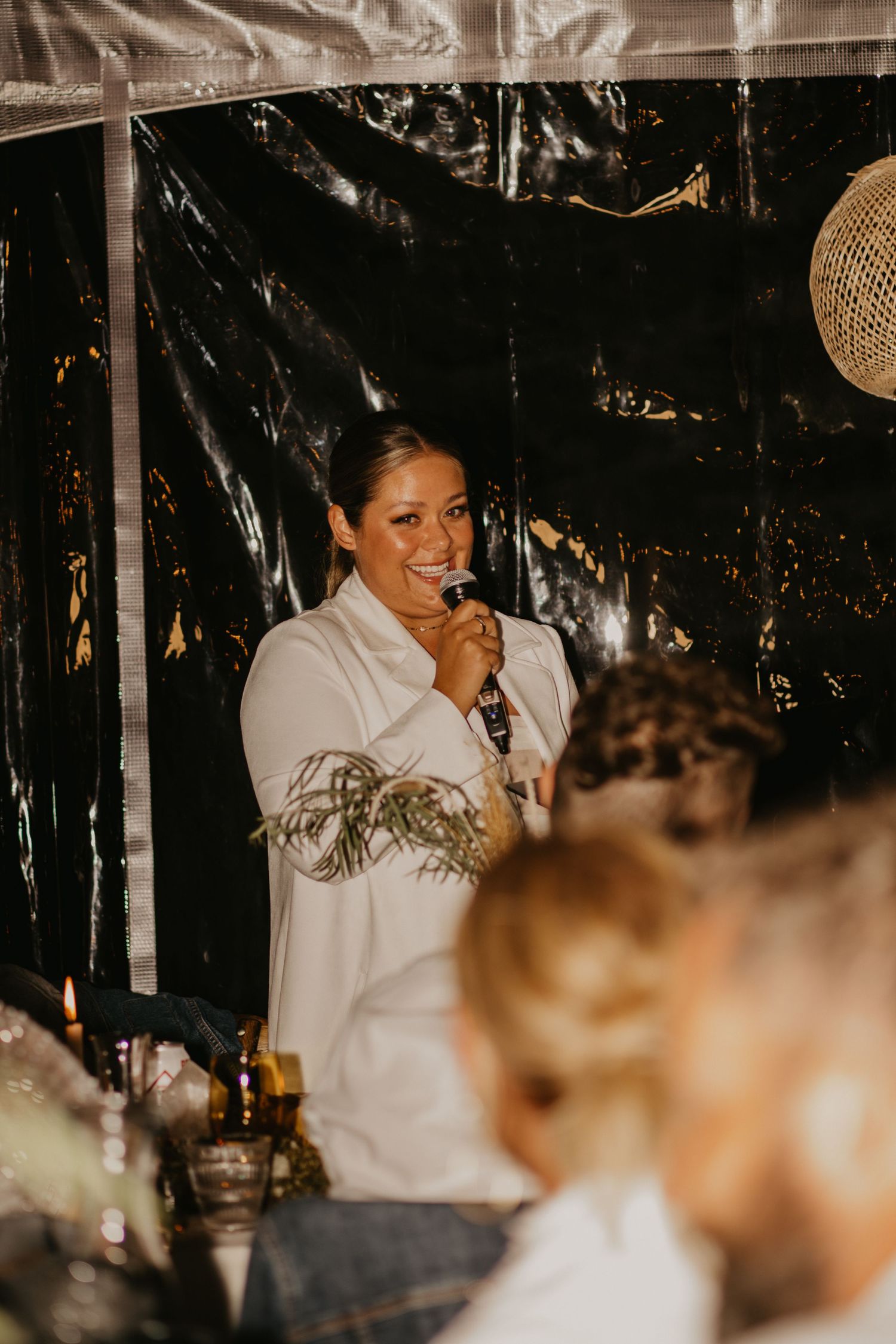 An indoor reception scene with a speaker in white against a dark backdrop.