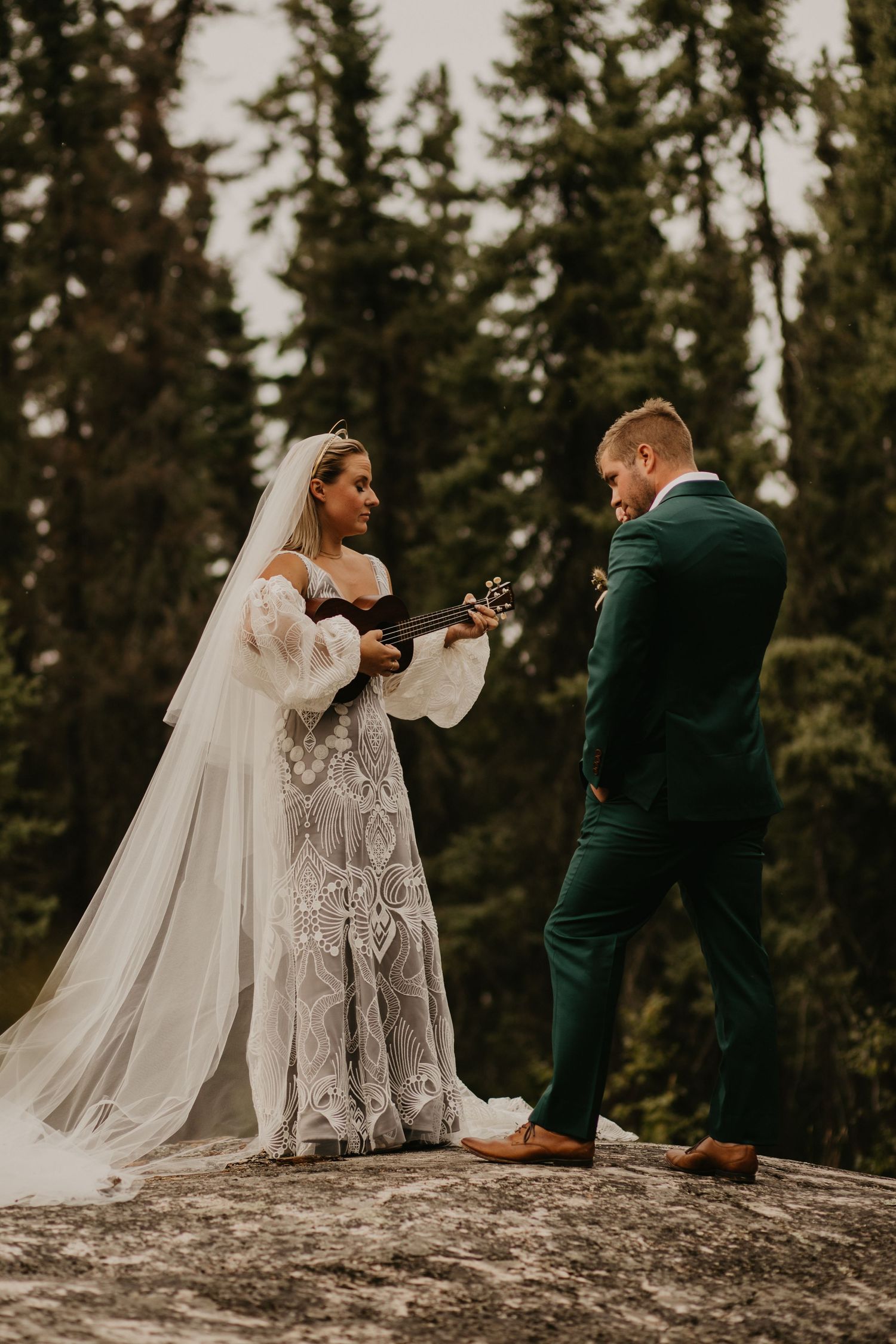 Couple exchanging wedding vows on rocky mountain outcrop surrounded by evergreen forest.