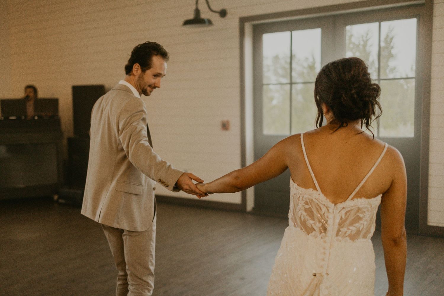 A couple holding hands during their first dance in a rustic barn venue.