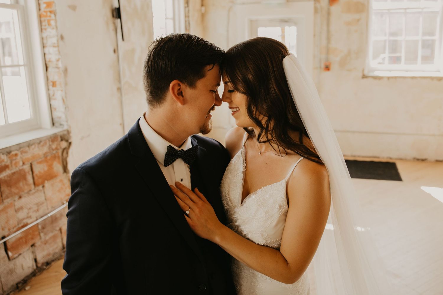 A romantic wedding couple shares an intimate moment in a bright industrial venue.