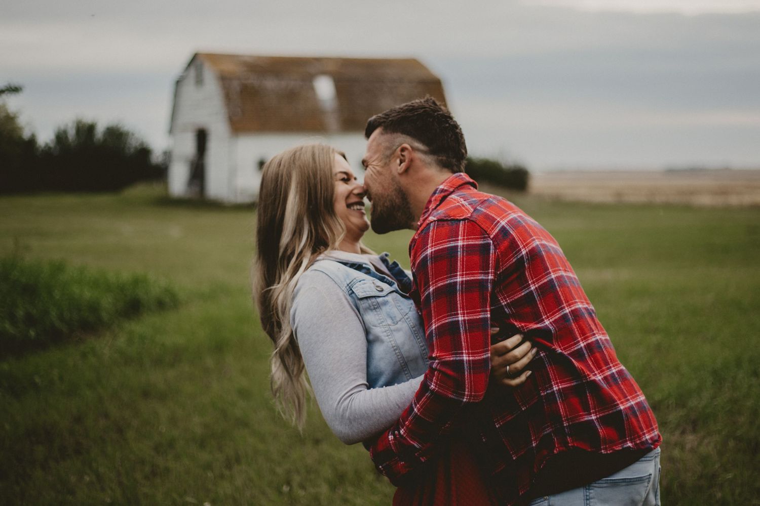 A romantic couple's portrait against a rustic white barn in golden light.