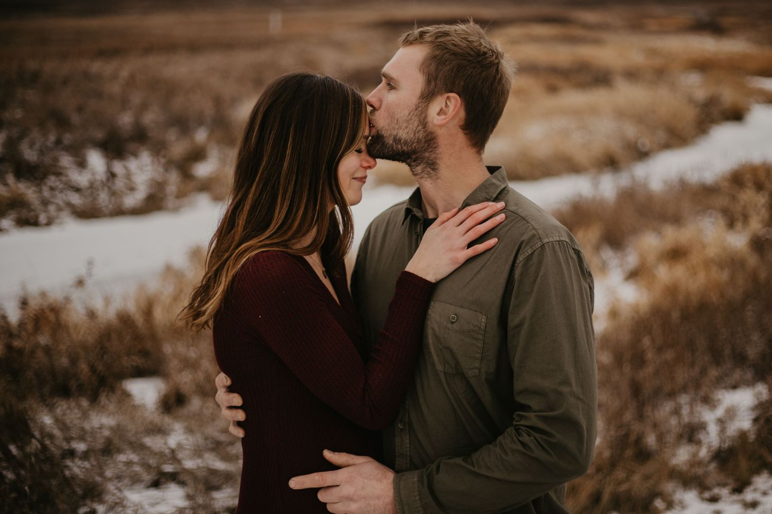 A romantic couple shares an intimate moment against a winter landscape backdrop.