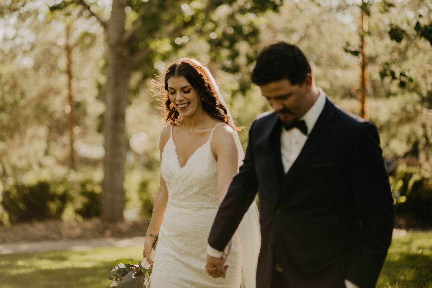 Newlyweds sharing a joyful moment while walking through a sun-dappled garden.