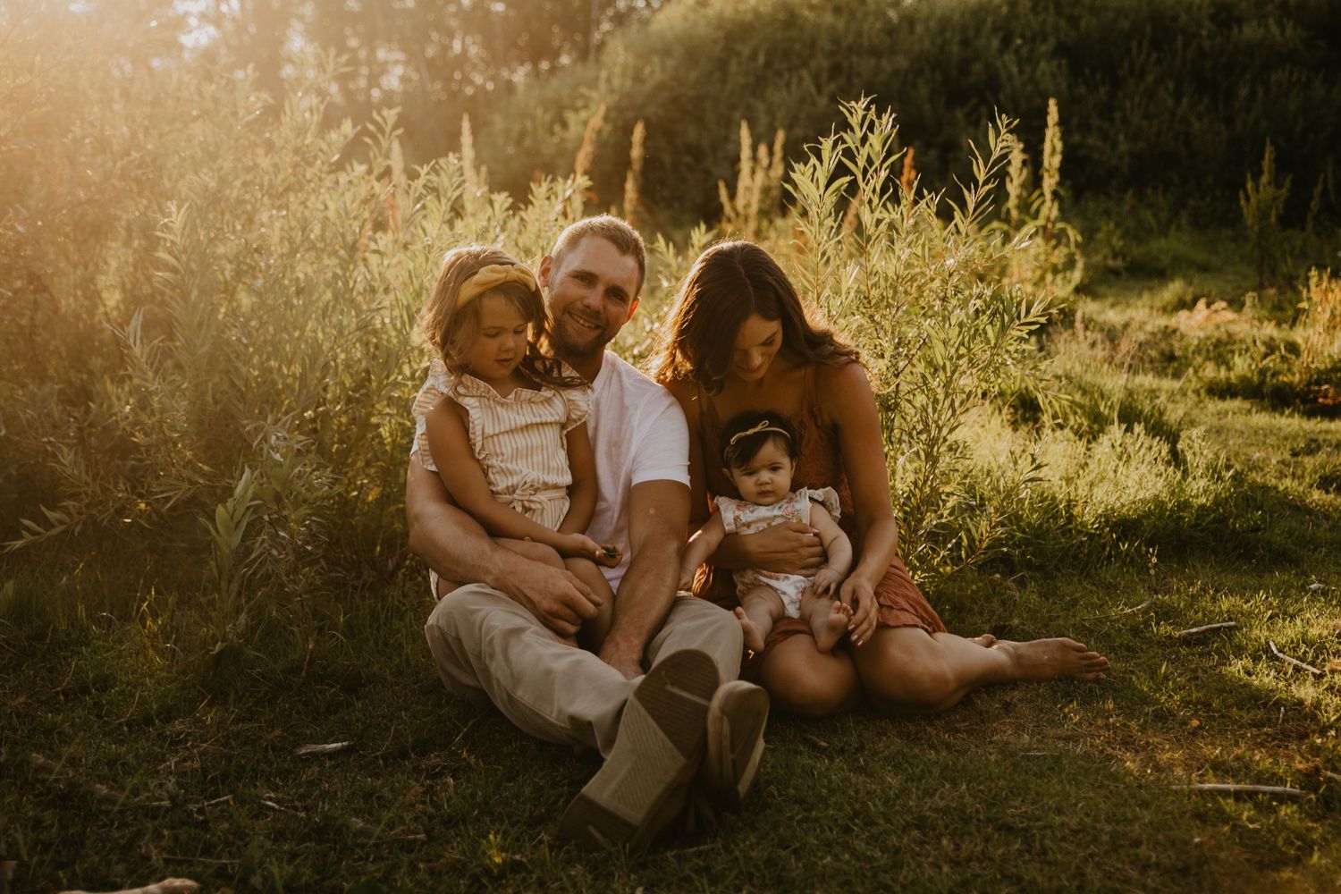 A family sits together in a sunlit meadow during golden hour.