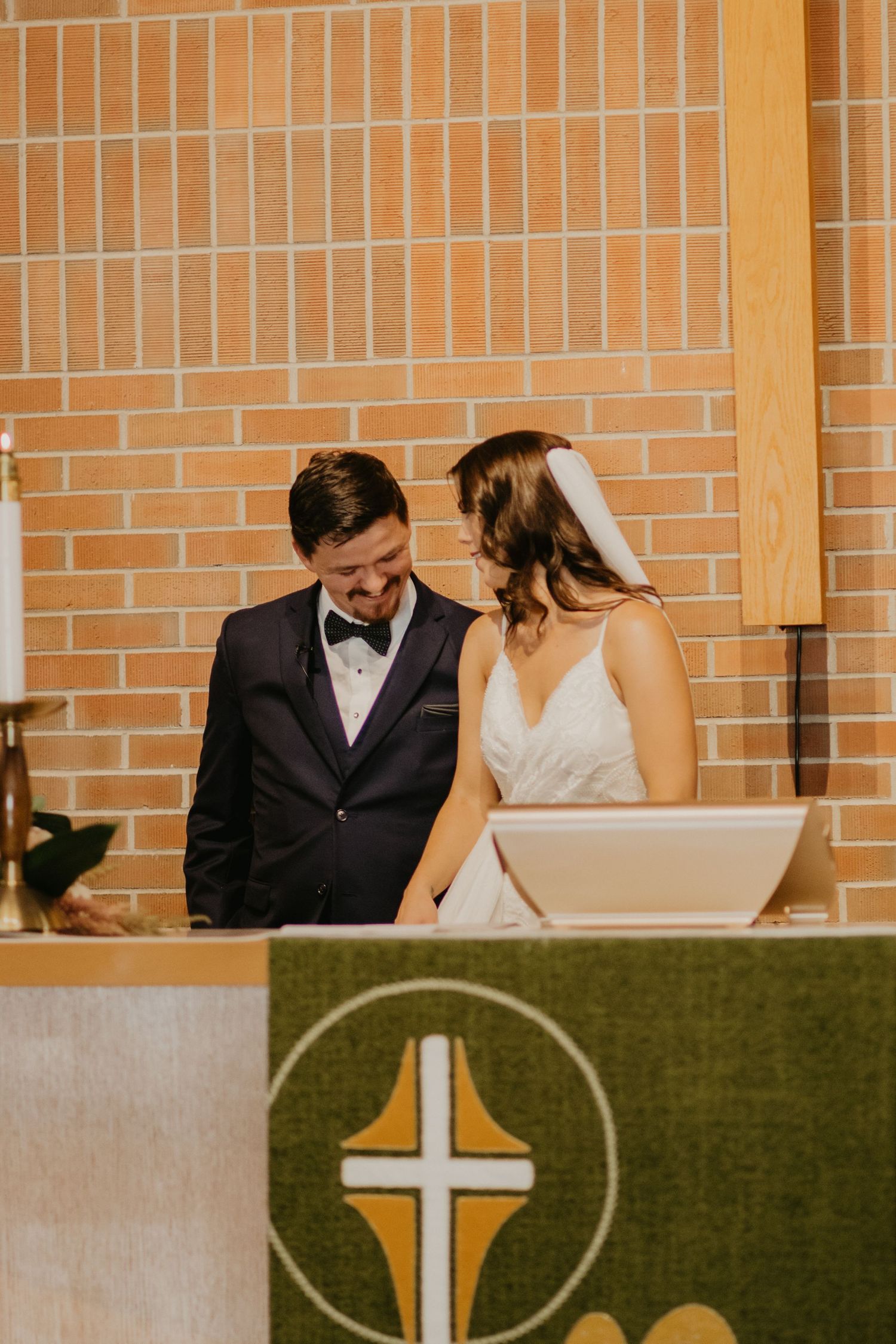 A couple stands at a church altar with a cross symbol during their wedding ceremony.