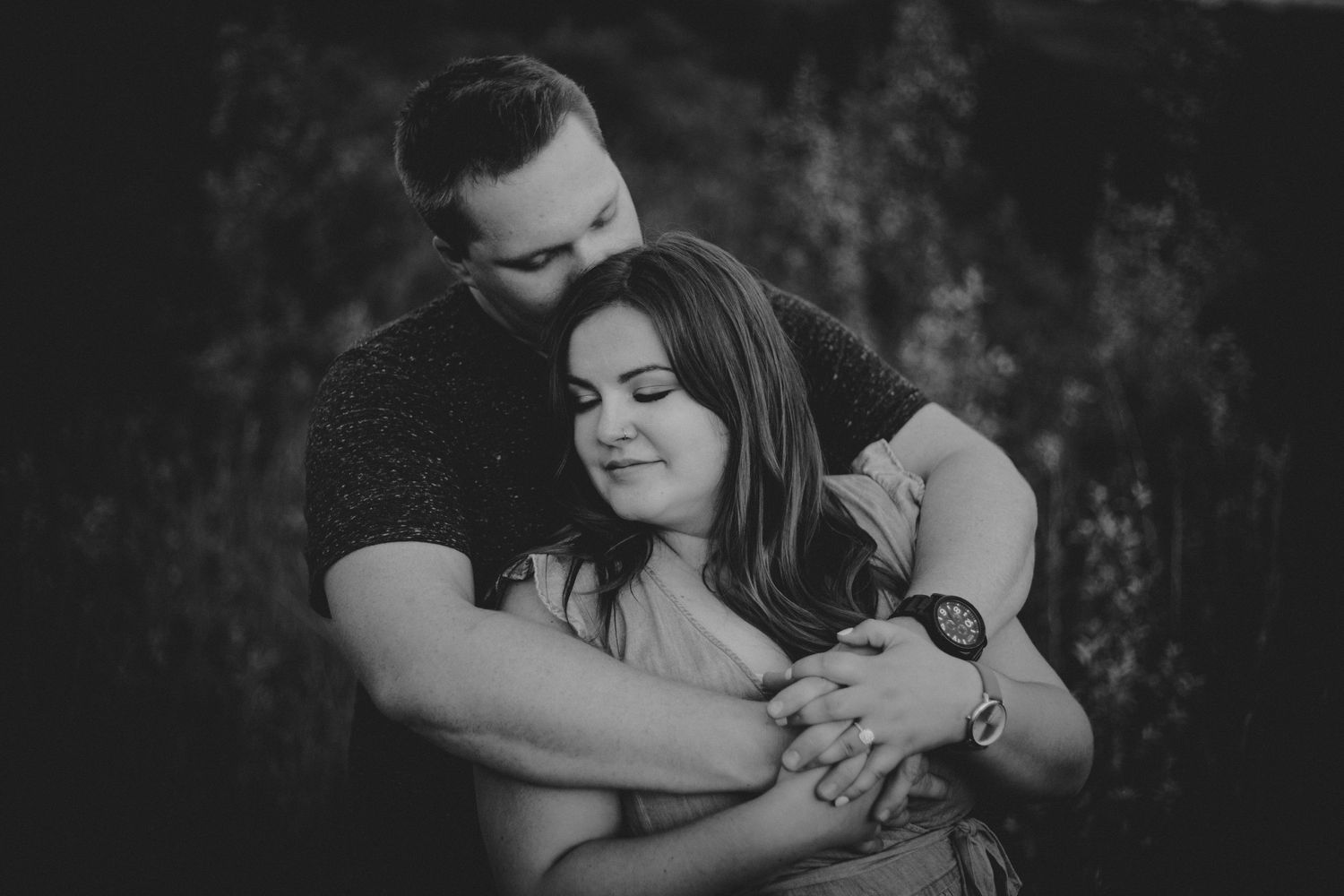 An intimate black and white portrait of a couple embracing in soft focus.