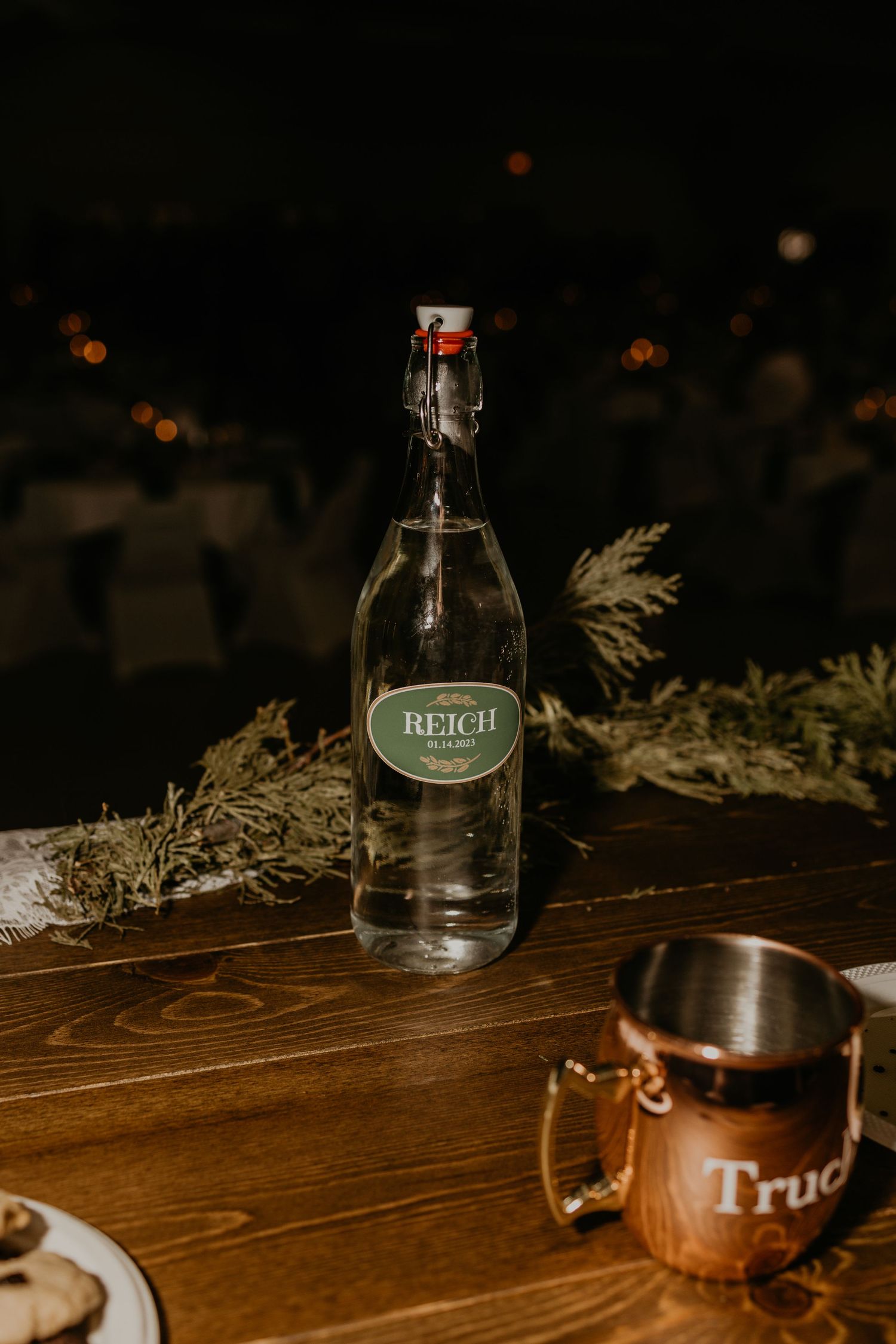A Beich glass bottle and copper mug on a rustic wooden table with moody lighting.