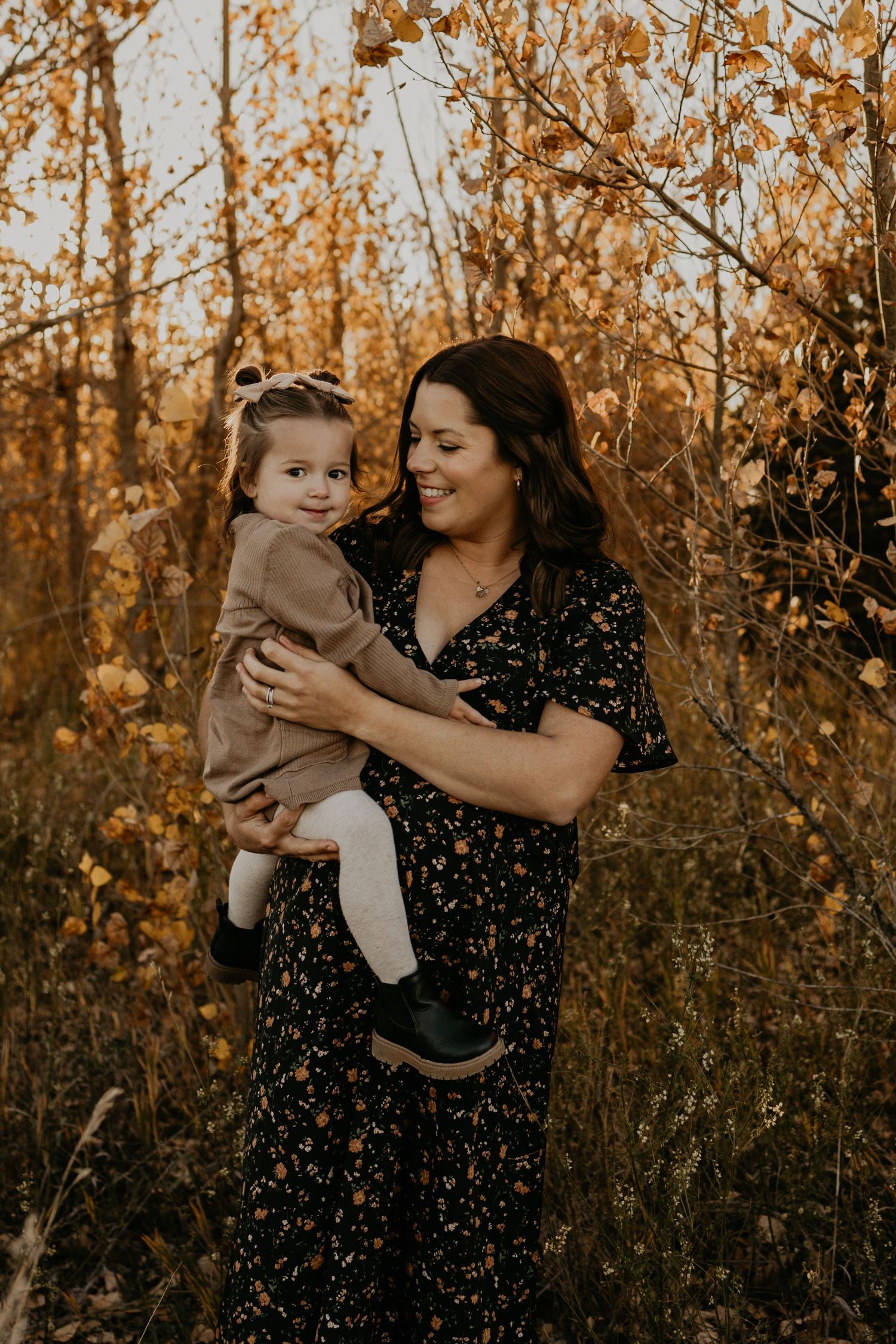 Mother and child share tender moment in golden autumn field at sunset.