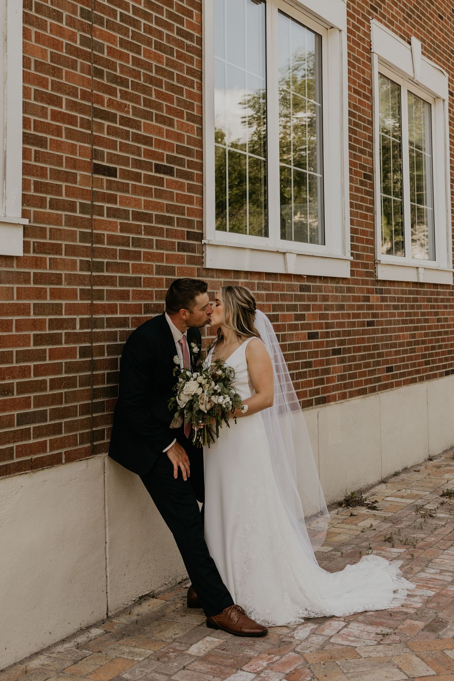 A tender wedding moment shared between newlyweds against a classic brick building backdrop.