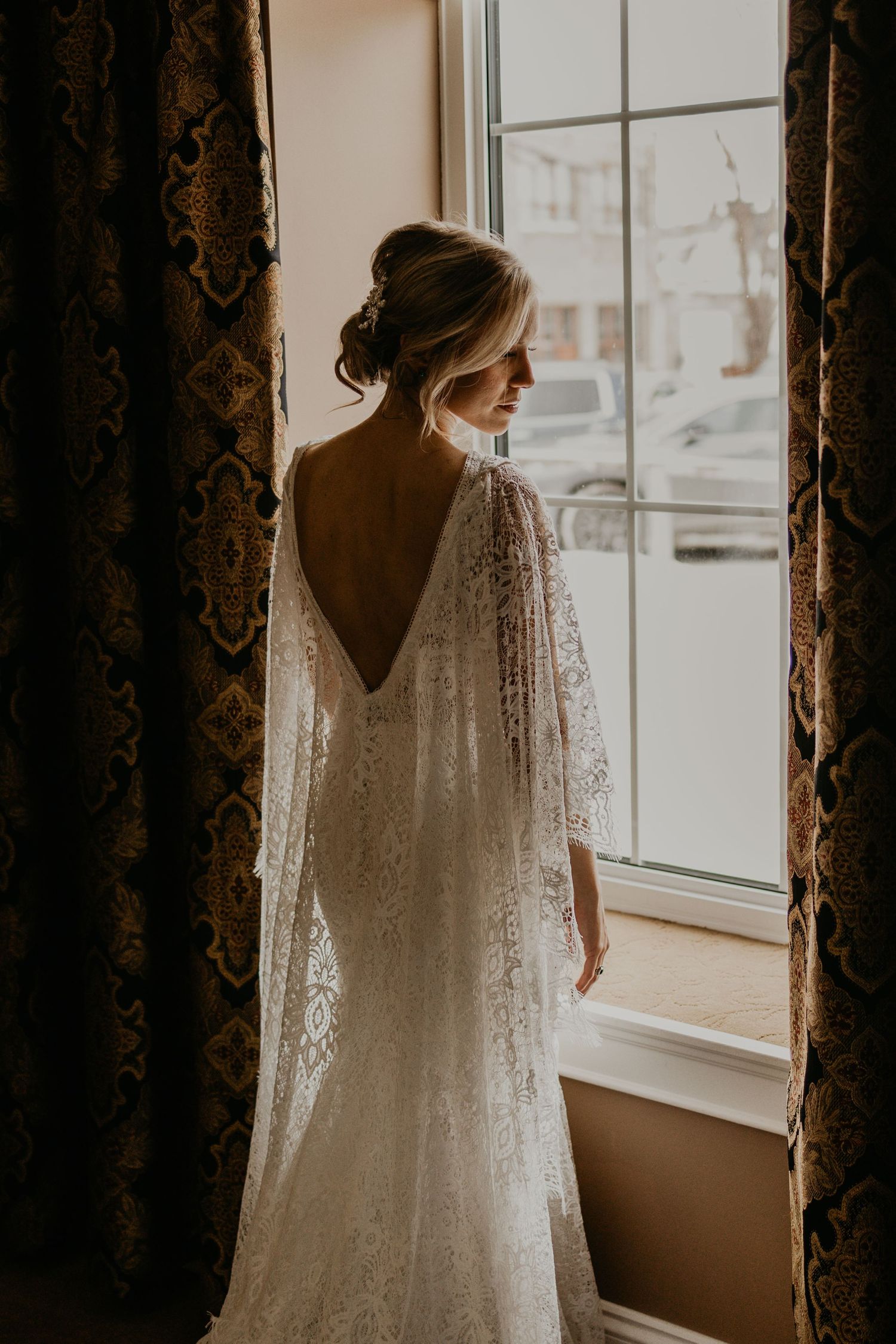 An elegant wedding dress with deep V-back and lace sleeves shown in soft window light.