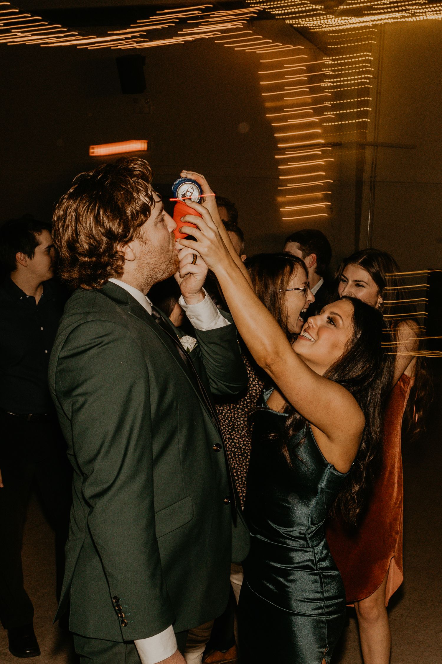 Party guests share drinks and dance at dimly lit reception venue.