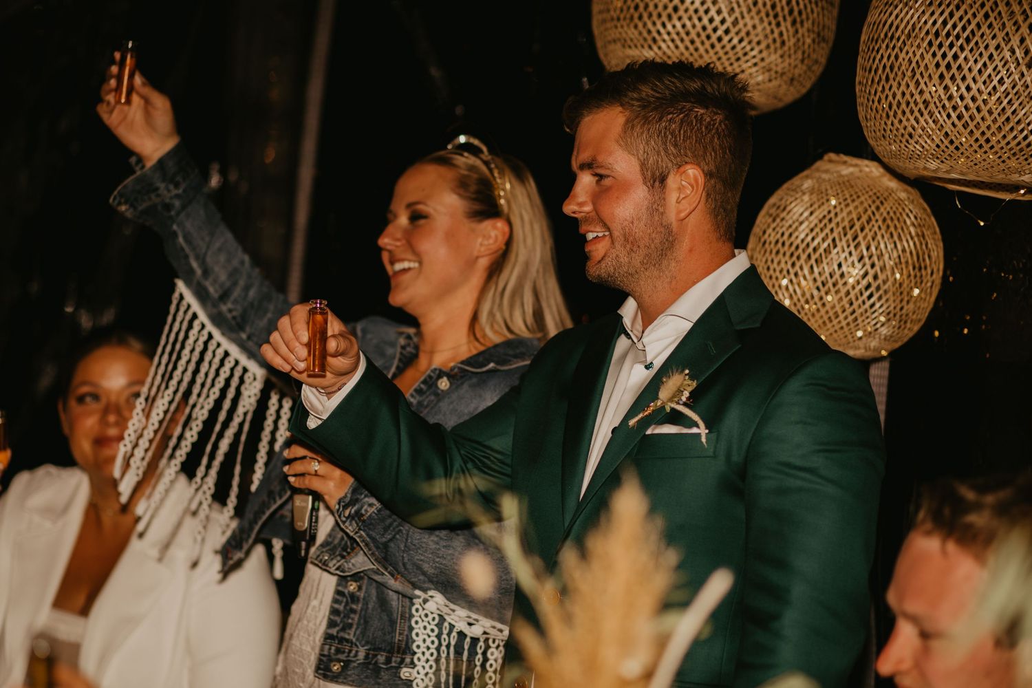 Couple celebrating at wedding reception with raised hands under decorative hanging lights.